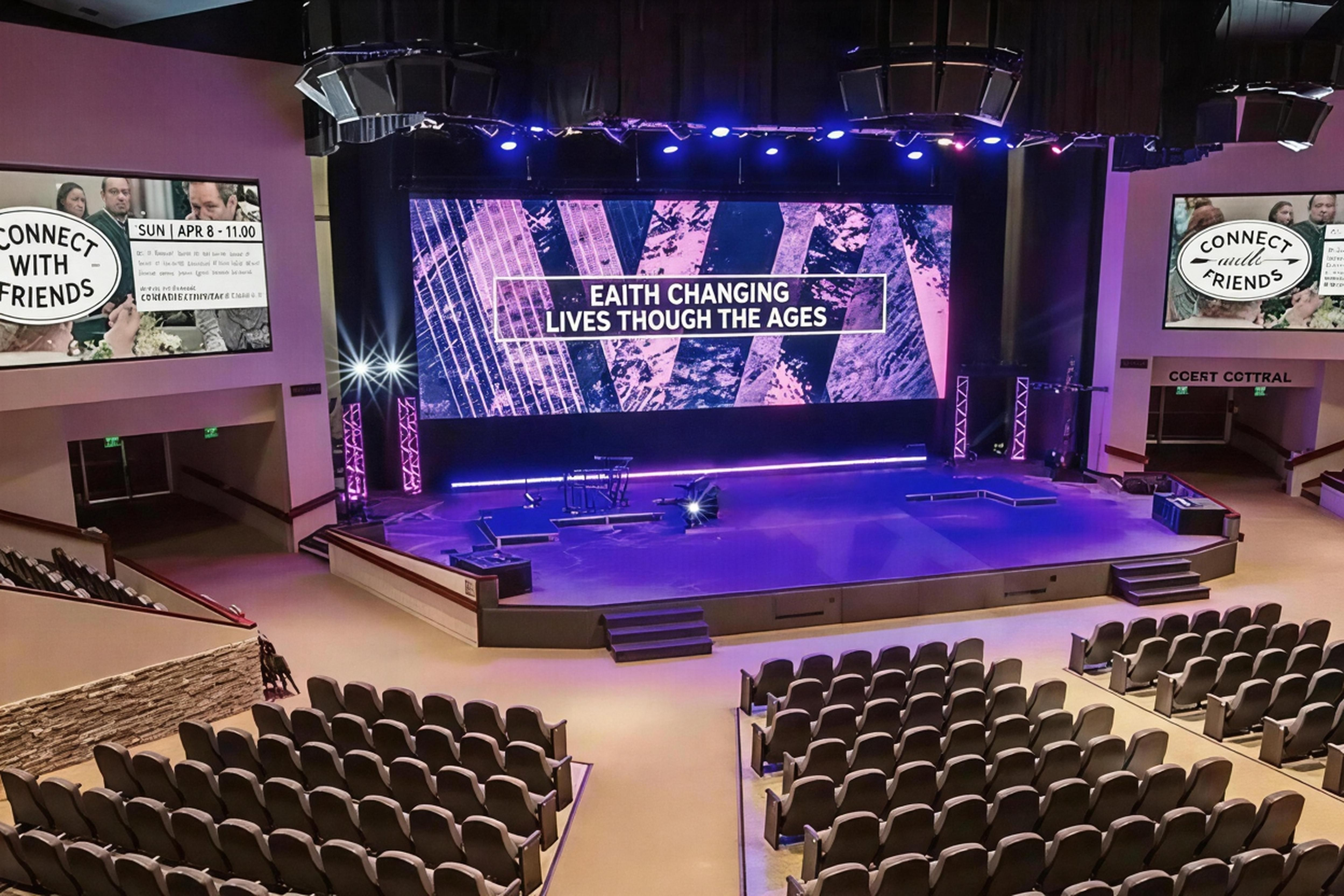Interior of a conference hall with a stage and large screens displaying the words 'Faith Changing Lives Through the Ages,' with seating arranged in front, ready for an event.