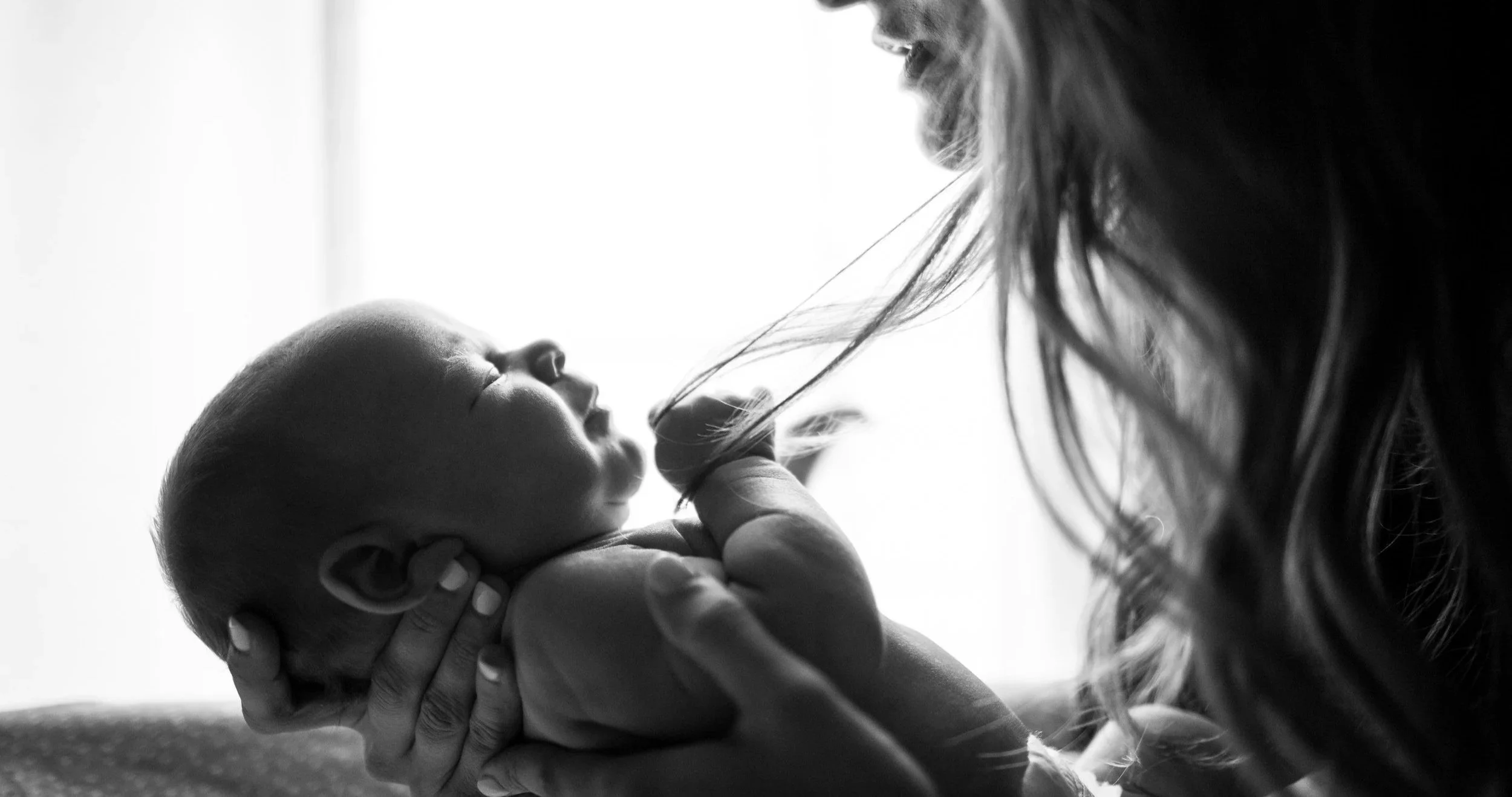 A woman holding a sleeping newborn baby close to her face in black and white.