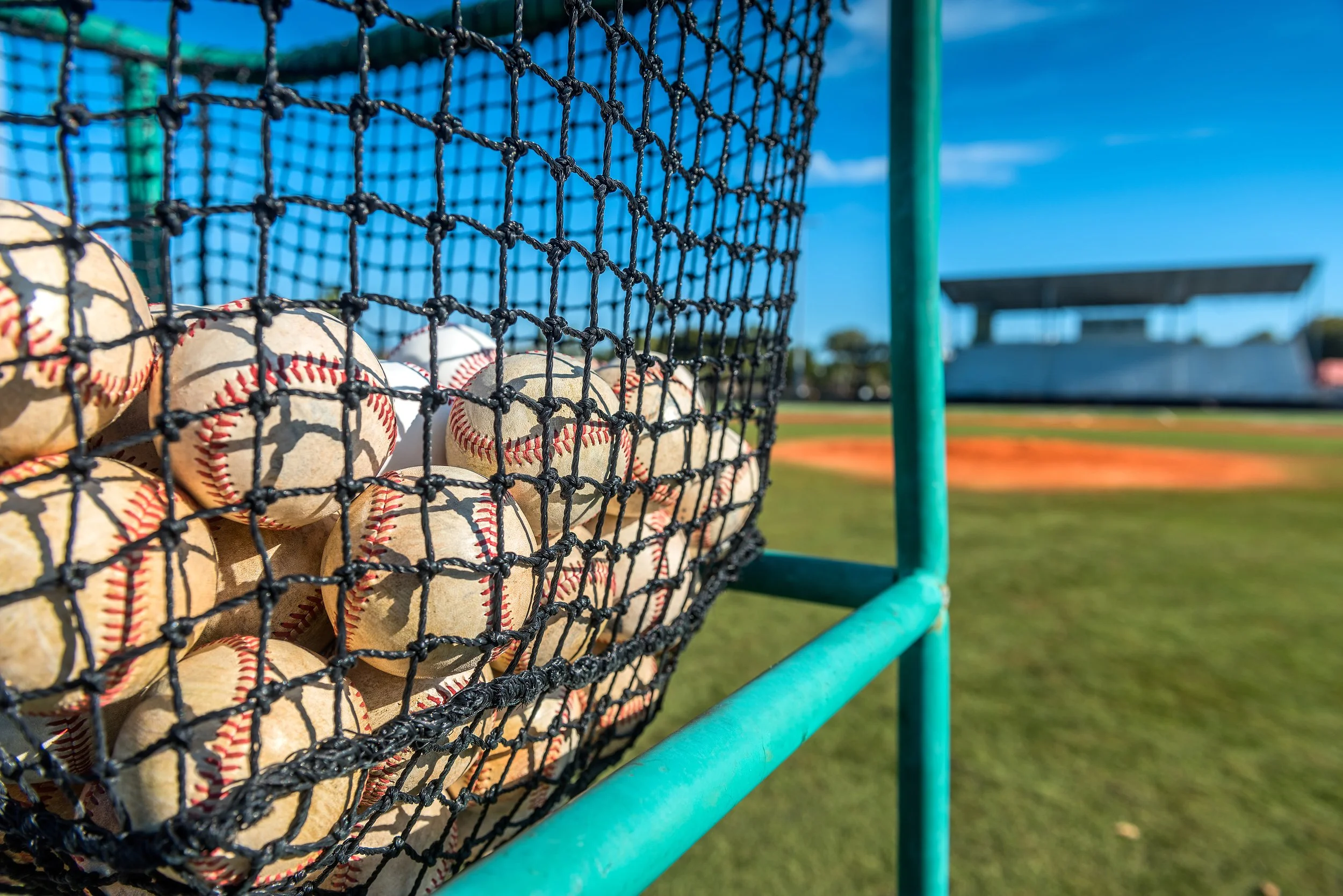 A baseball net filled with multiple baseballs on a baseball field.