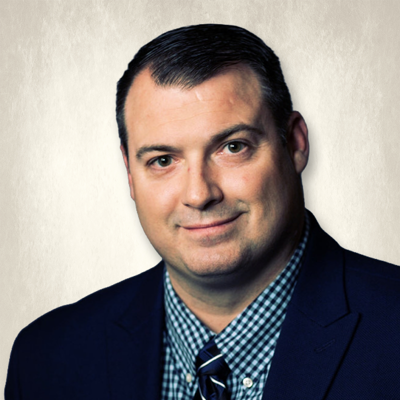 Headshot of a man in a suit and tie smiling against a plain background.