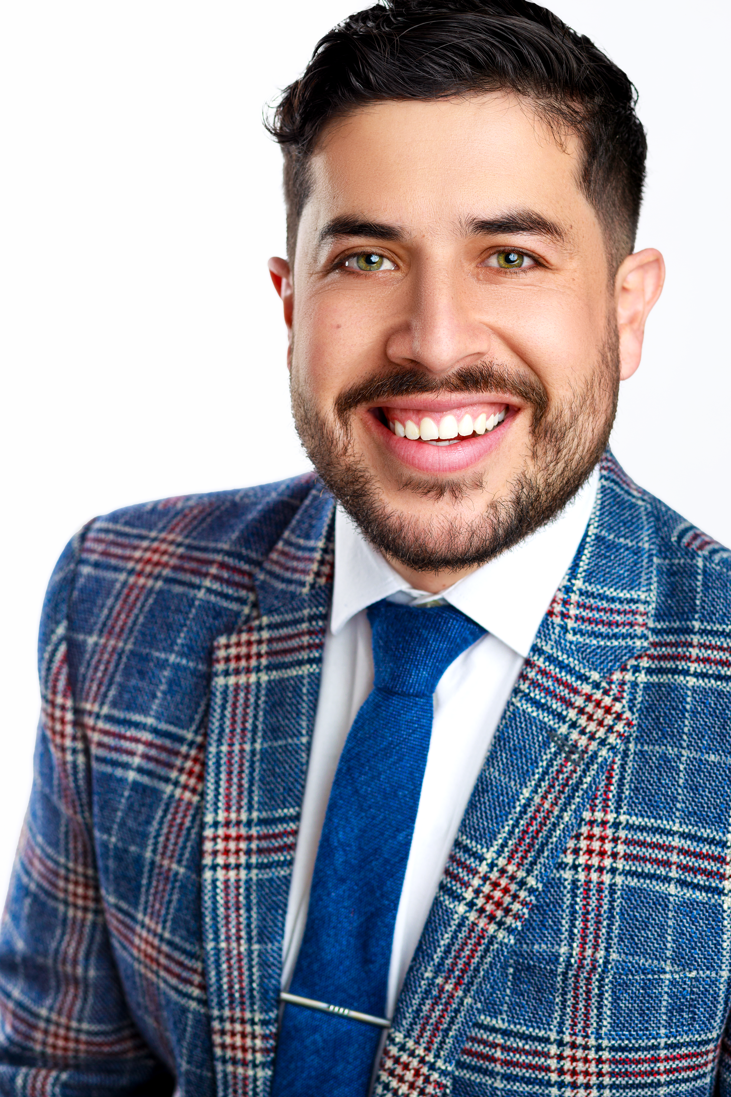 Portrait of a smiling man wearing a plaid suit jacket, white shirt, and blue tie, with a white background.