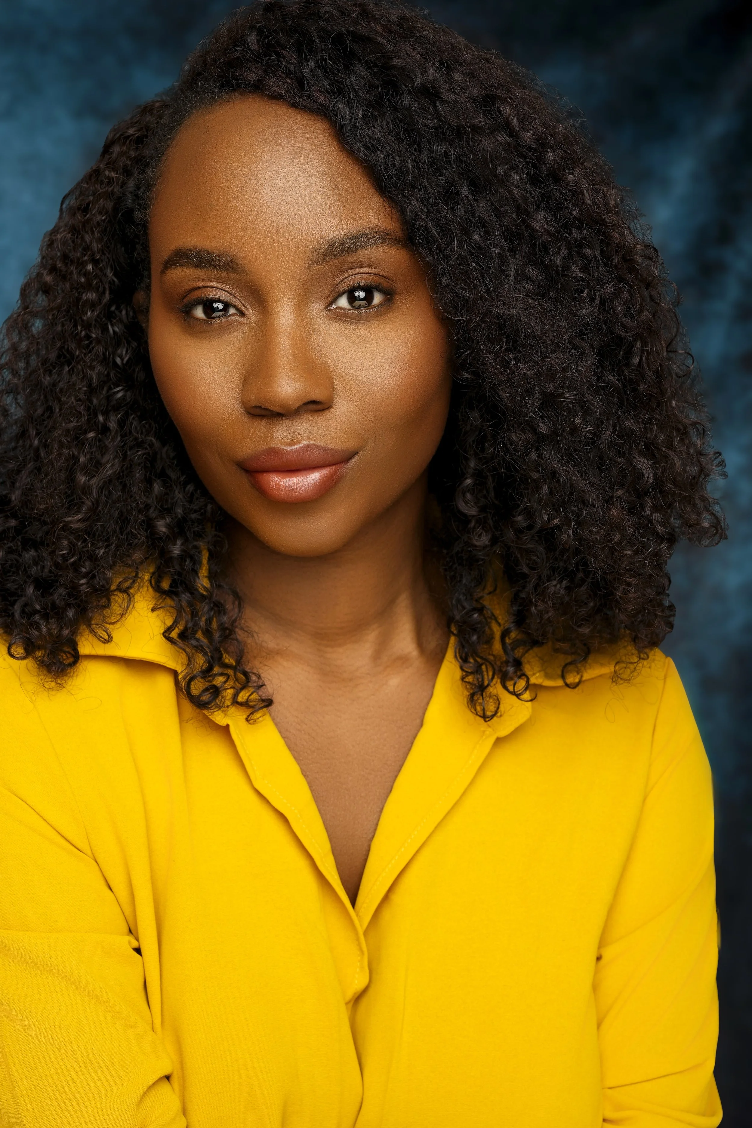 A portrait of a woman with curly dark hair, wearing a yellow blouse, against a blue textured background.