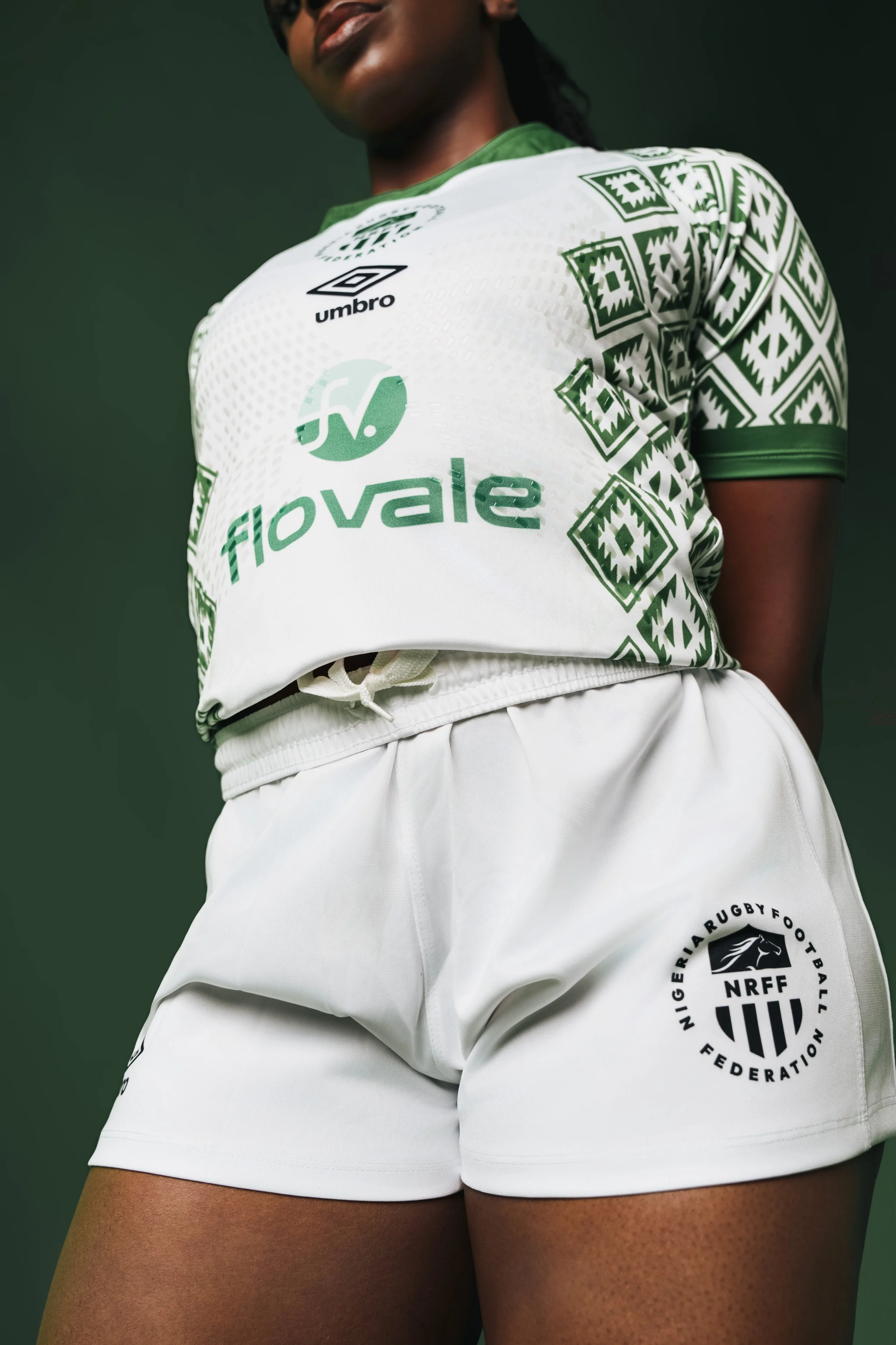 Close-up of a female athlete wearing a white and green Nigeria rugby team jersey and white shorts with the Nigeria Rugby Football Federation logo, against a dark green background.