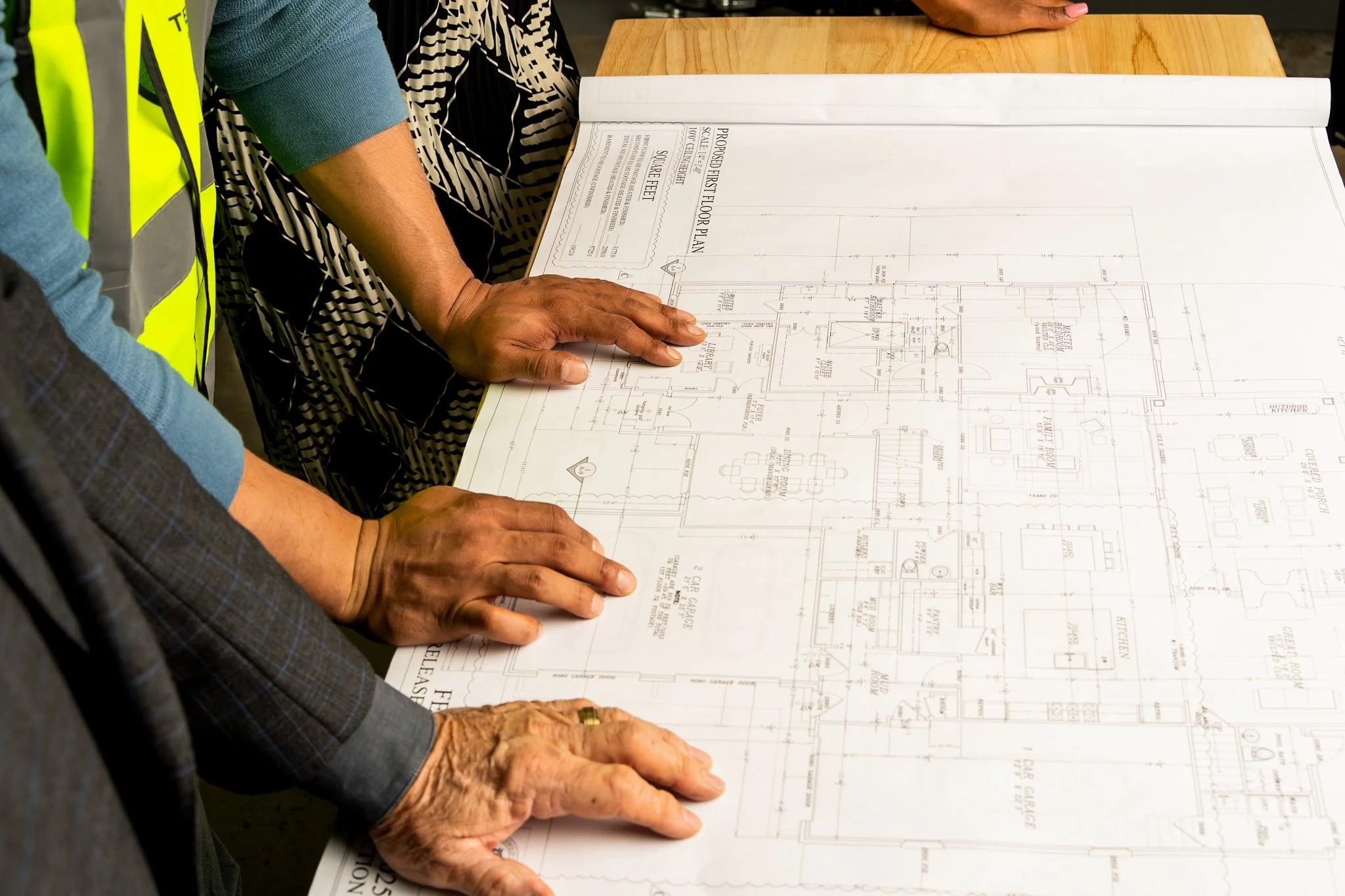 Two individuals examining a large architectural blueprint on a wooden table.