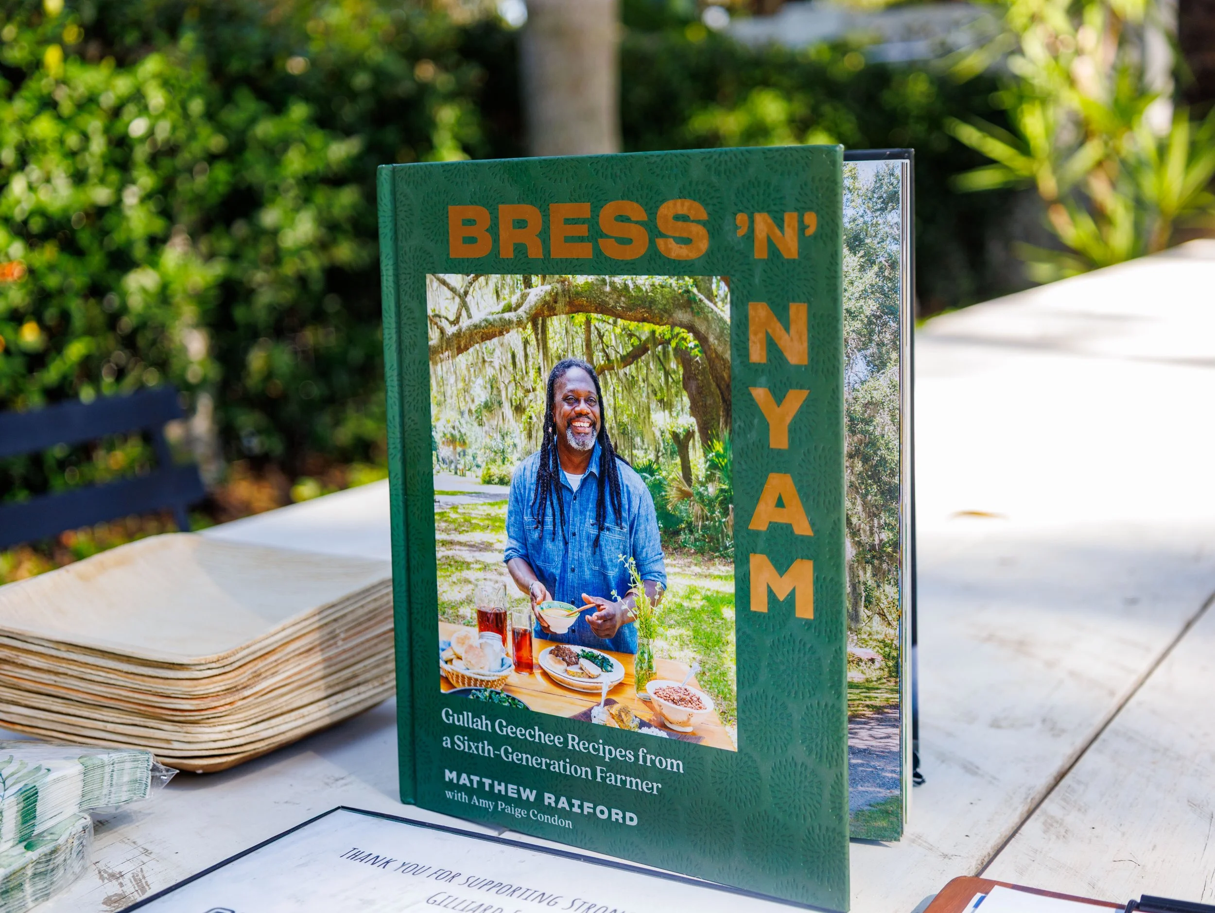 Cookbook titled "Bress 'N' Nyam" by Matthew Raiford with Amy Paige Condon. The cover features a photo of a man with dreadlocks, wearing a blue denim shirt, standing outdoors under a large tree, with a table of food in front of him.