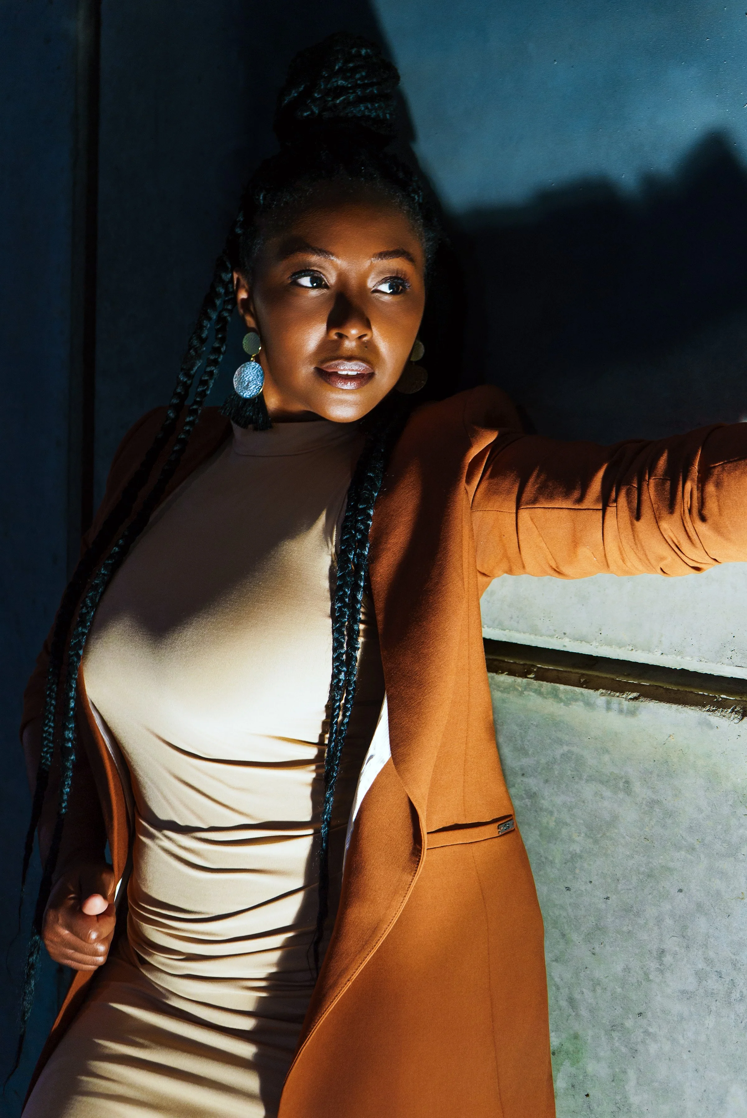 A woman with styled cornrows and large earrings takes a selfie against a gray wall.