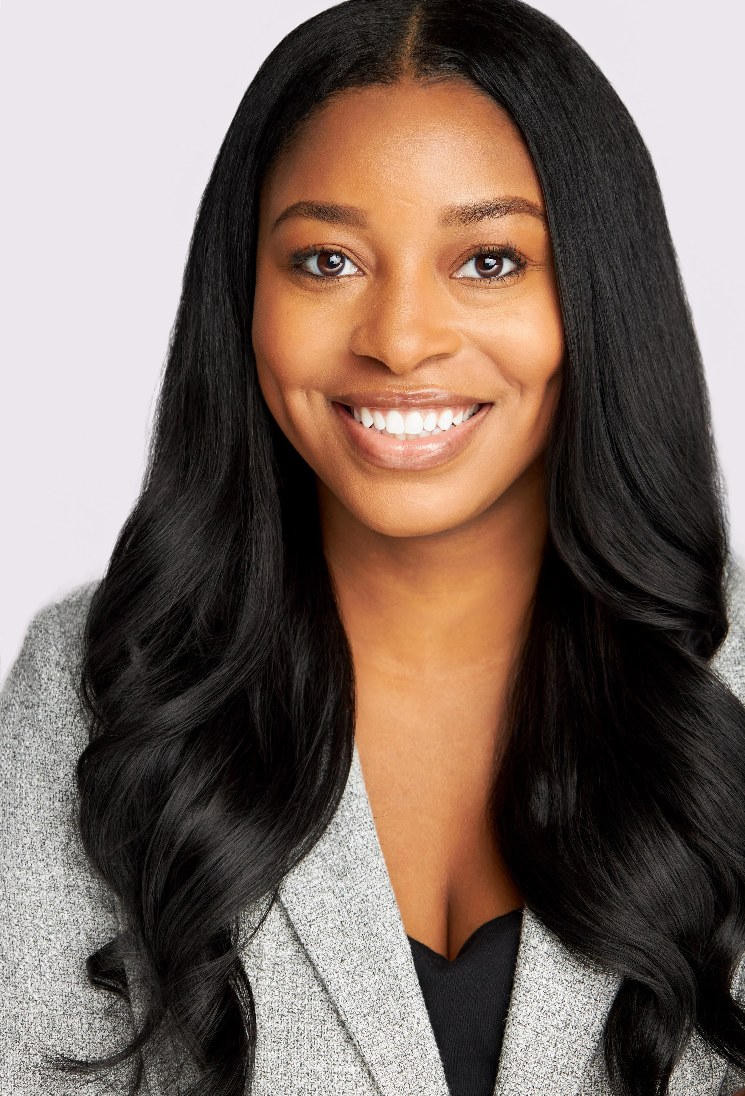 A smiling woman with long black hair, wearing a gray blazer, against a light background.