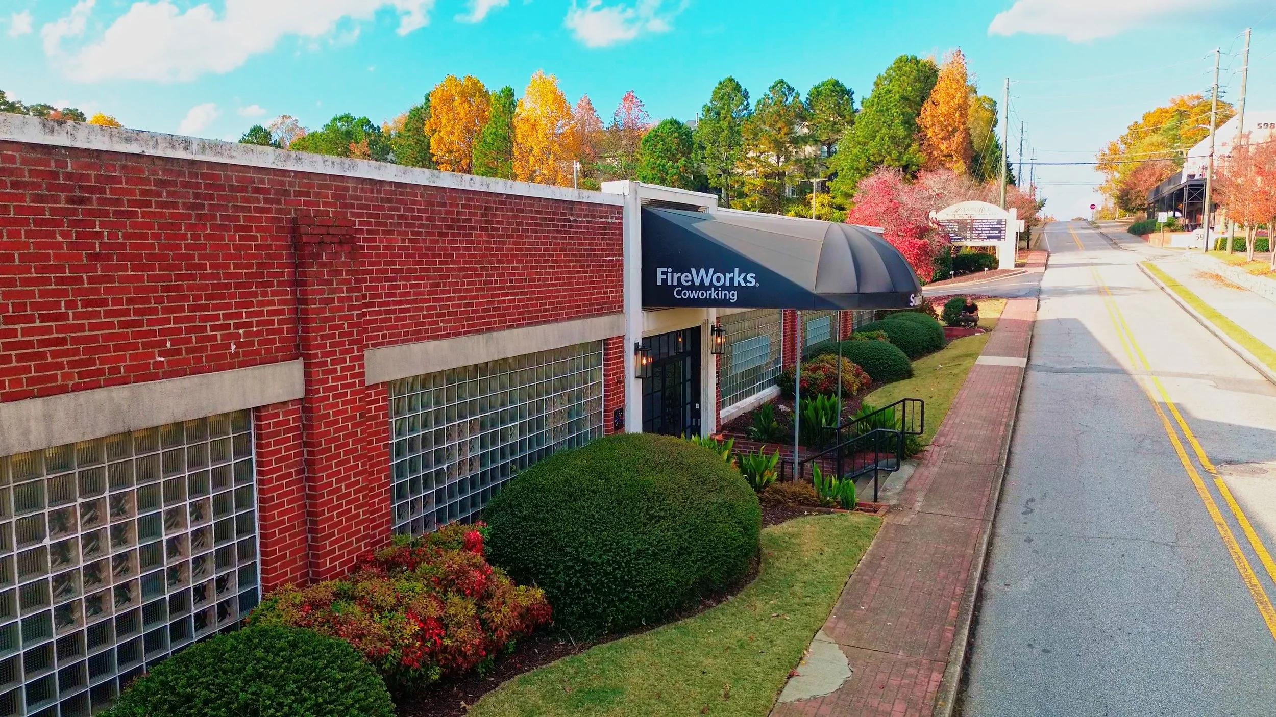 Street view of a brick building with a sign that says 'FireWorks Coworking', surrounded by colorful autumn trees and shrubs.