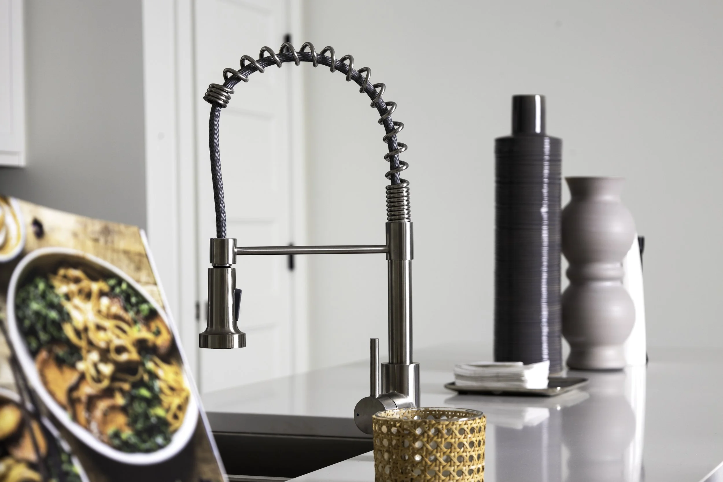 Modern kitchen sink with a high-arc spring faucet, a board with food pictures, and decorative vases in neutral colors.