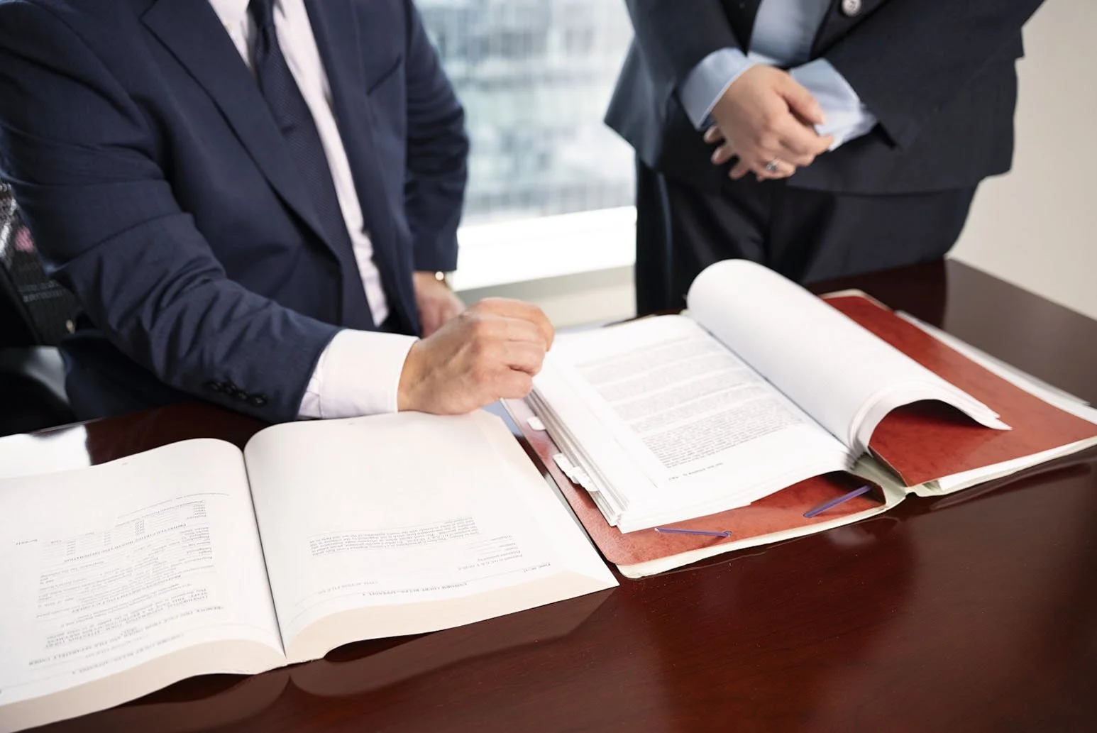 Business professionals reviewing legal documents or contracts on a wooden table in an office.