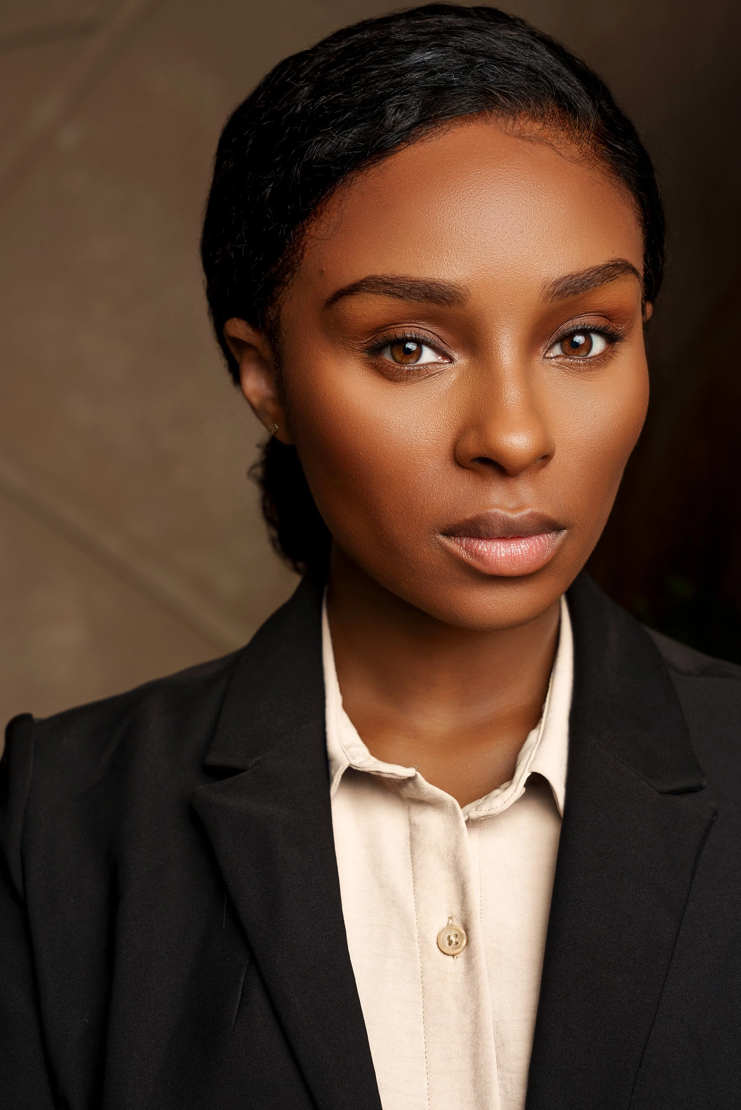 A professional woman with short black hair, brown eyes, wearing a black blazer and a beige button-up shirt, looking directly at the camera.