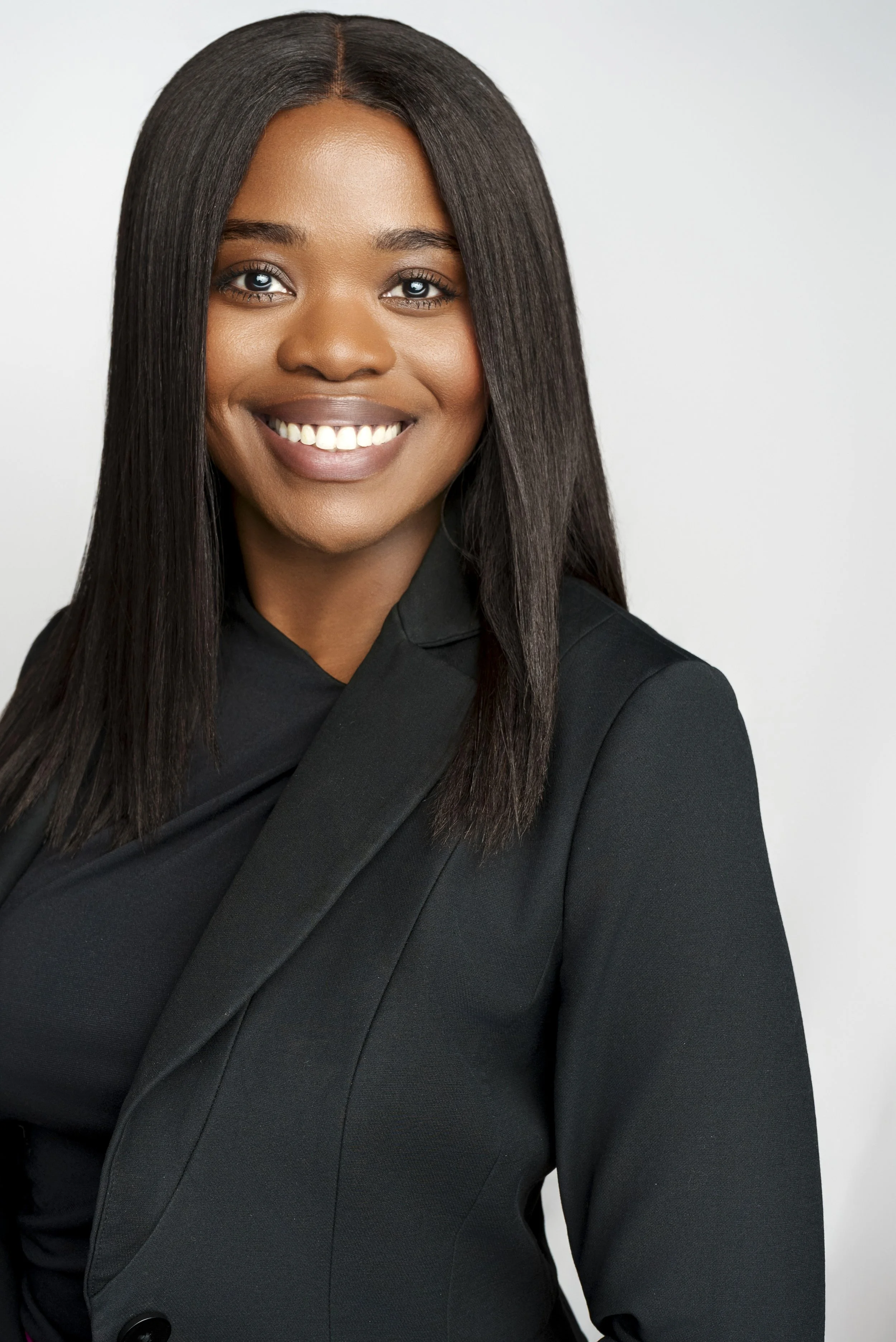 A smiling young woman with straight black hair wearing a black blazer against a plain light background.