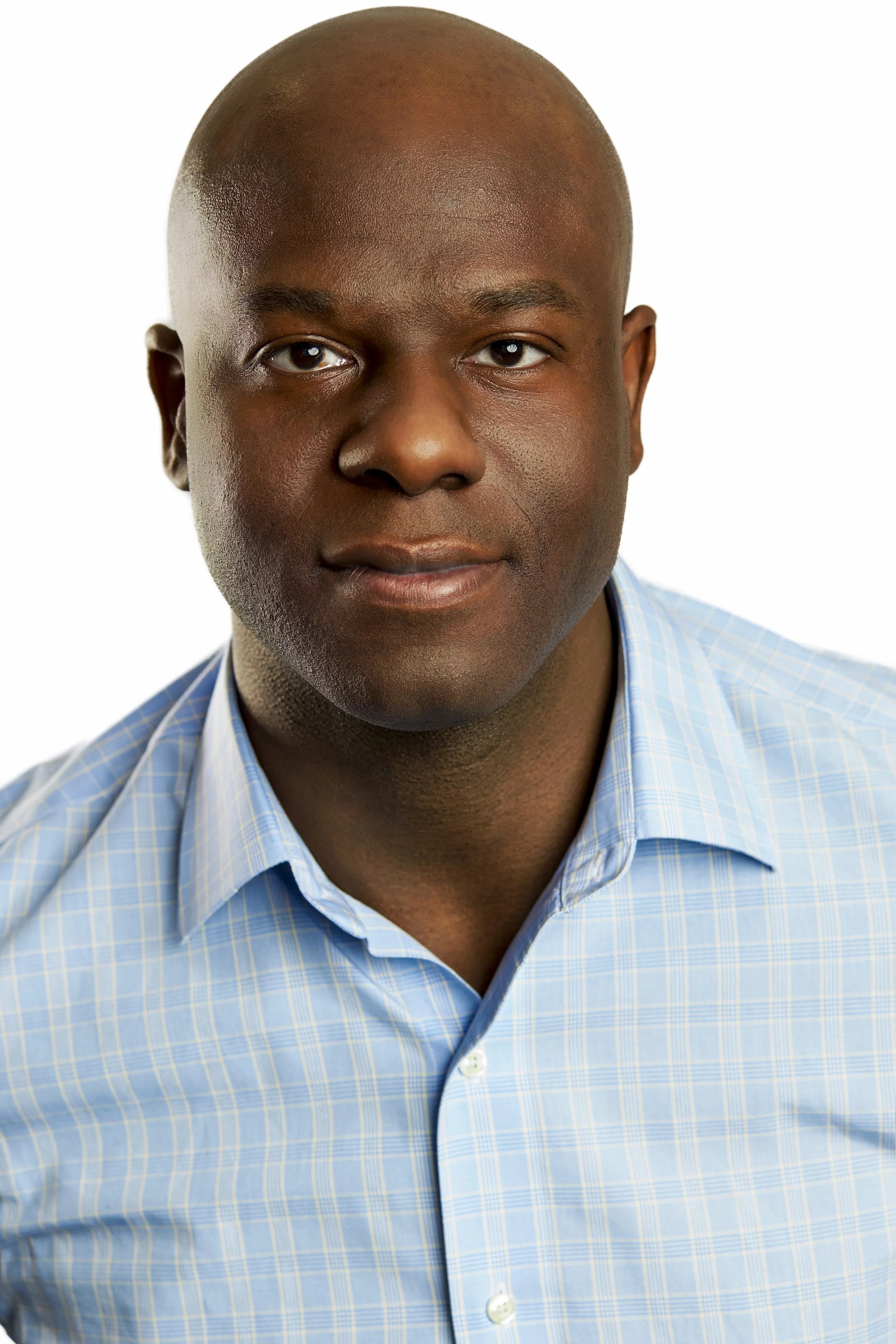 Close-up portrait of a middle-aged Black man with a shaved head, wearing a light blue checkered shirt, against a white background.