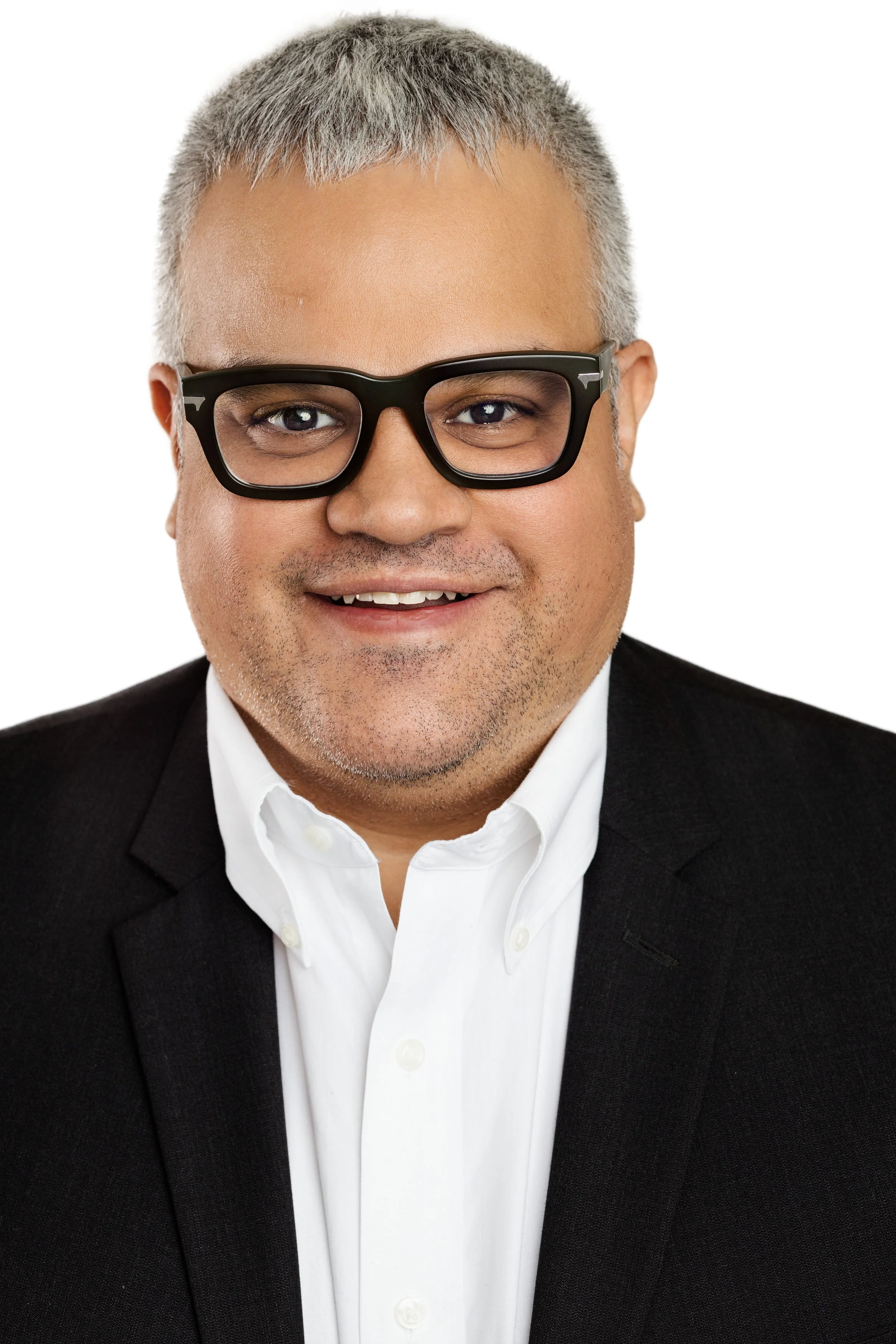 Headshot of a smiling man wearing black glasses, a white shirt, and a black suit blazer.