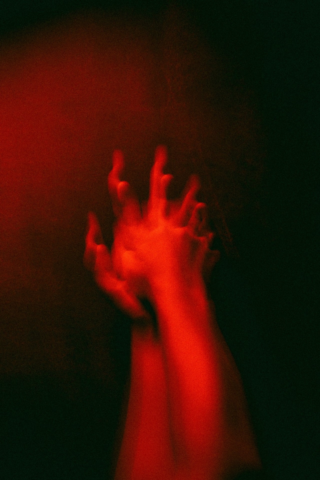 A pair of hands reaching upwards, illuminated with red and green lighting, against a dark background.