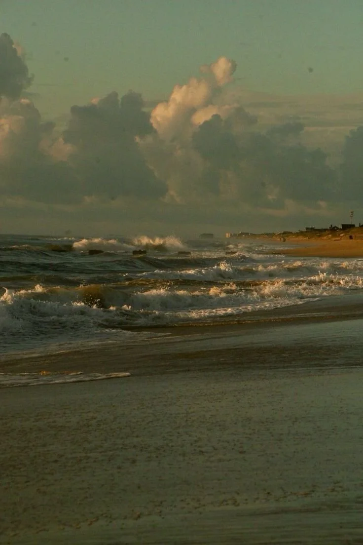 Beach scene with waves crashing on the shore and a cloudy sky overhead.