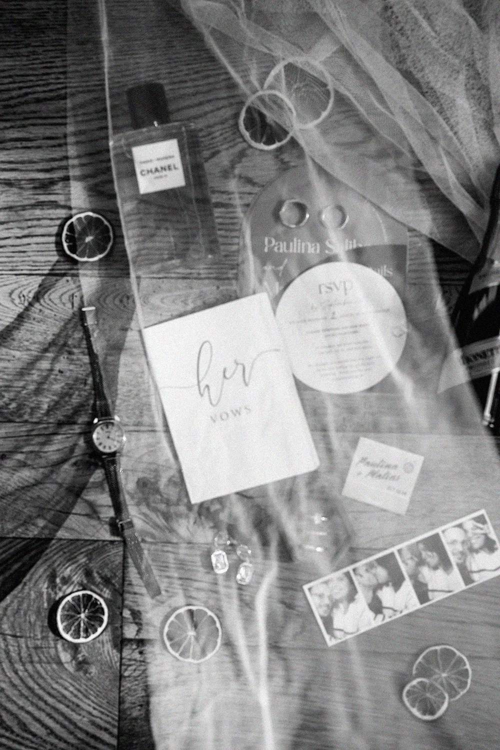 Flat lay of personal items on a wooden surface including perfume, watch, jewelry, a greeting card, and decorative slices of citrus.