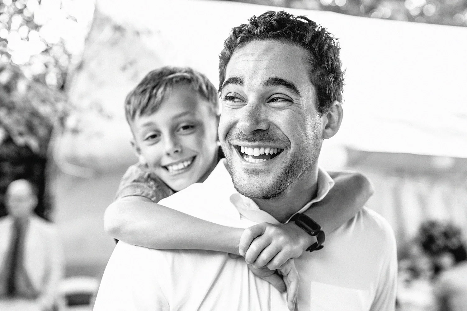 A man smiling and carrying a smiling boy on his back at an outdoor wedding in toronto