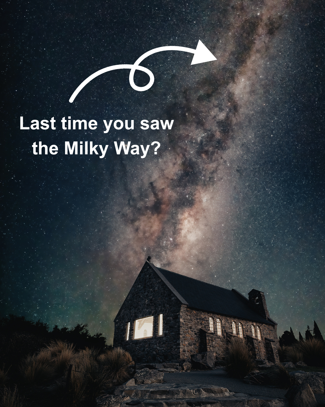 Night sky with stars and the Milky Way galaxy above a stone house with lit windows.