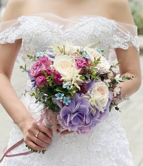 Bride in white lace wedding dress holding a colorful bouquet of roses and other flowers