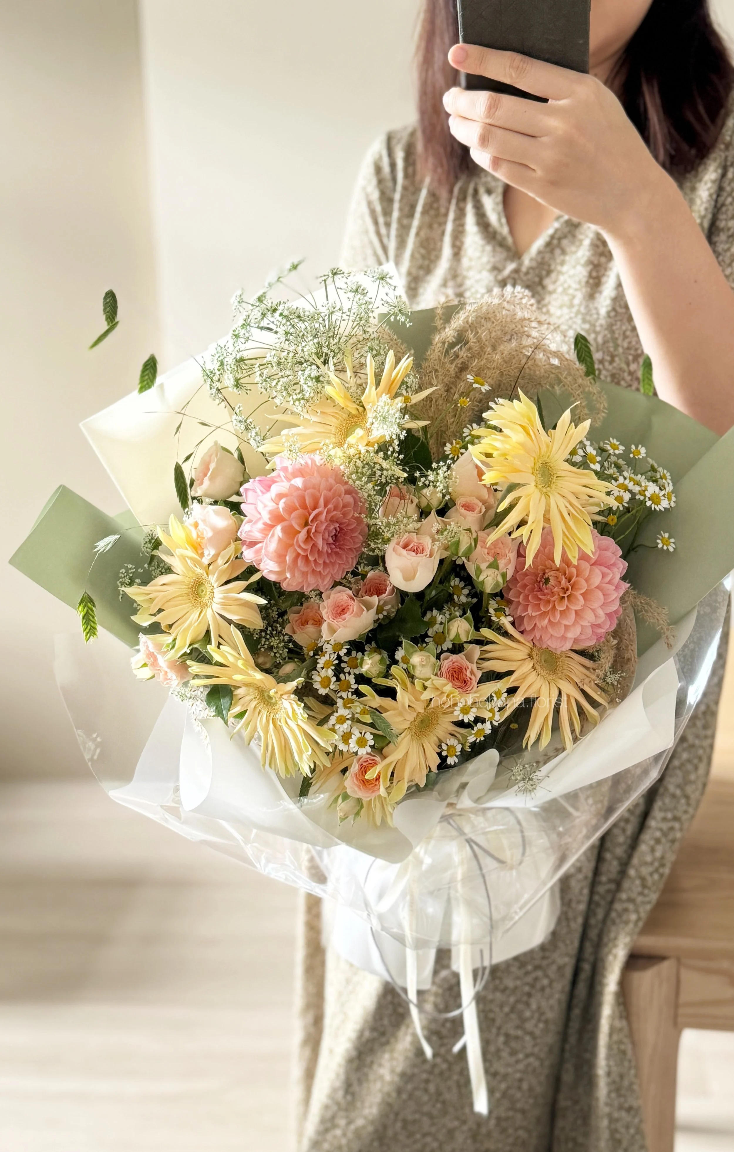 Person holding a bouquet of pink, yellow, and white flowers in a floral arrangement.