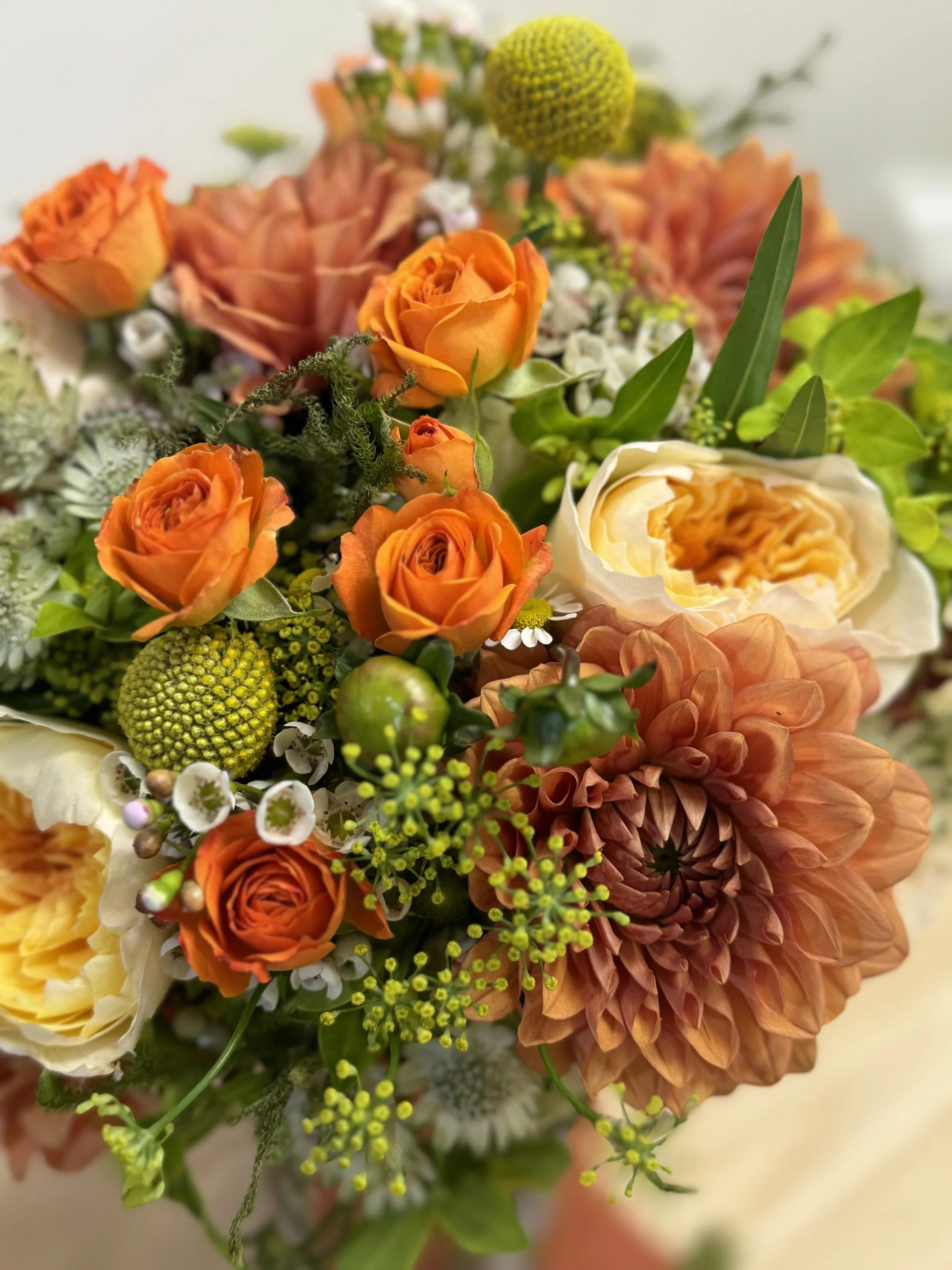 Close-up of a colorful bouquet of flowers including orange roses, white and peach peonies, green hypericum berries, and green foliage.