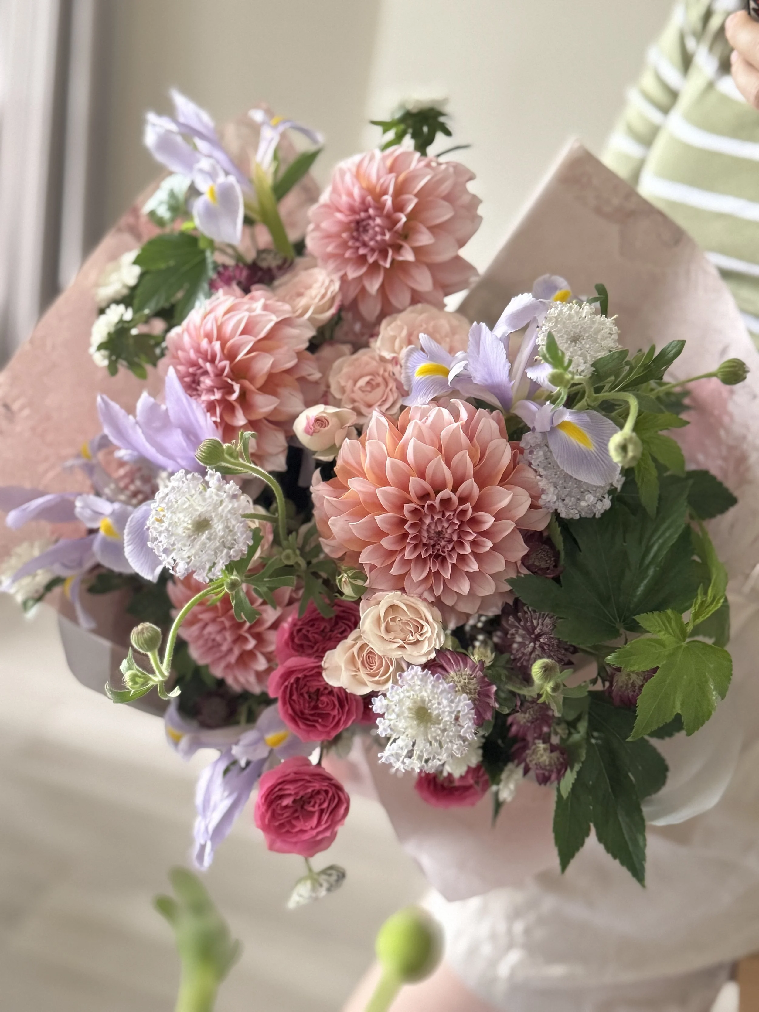 Bouquet of pink, purple, and white flowers wrapped in pink paper.