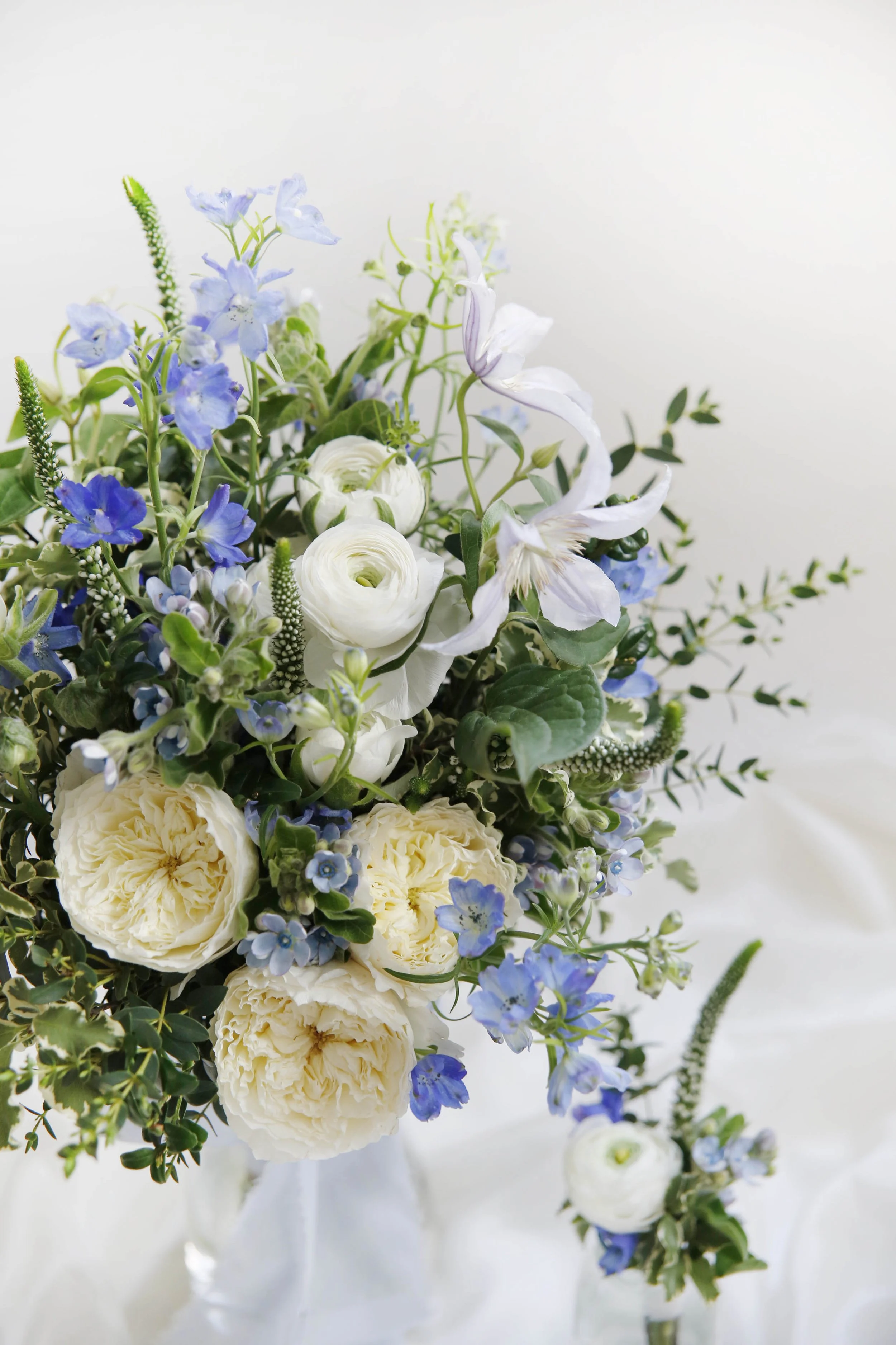 A bouquet of white and blue flowers with green foliage on a white background.