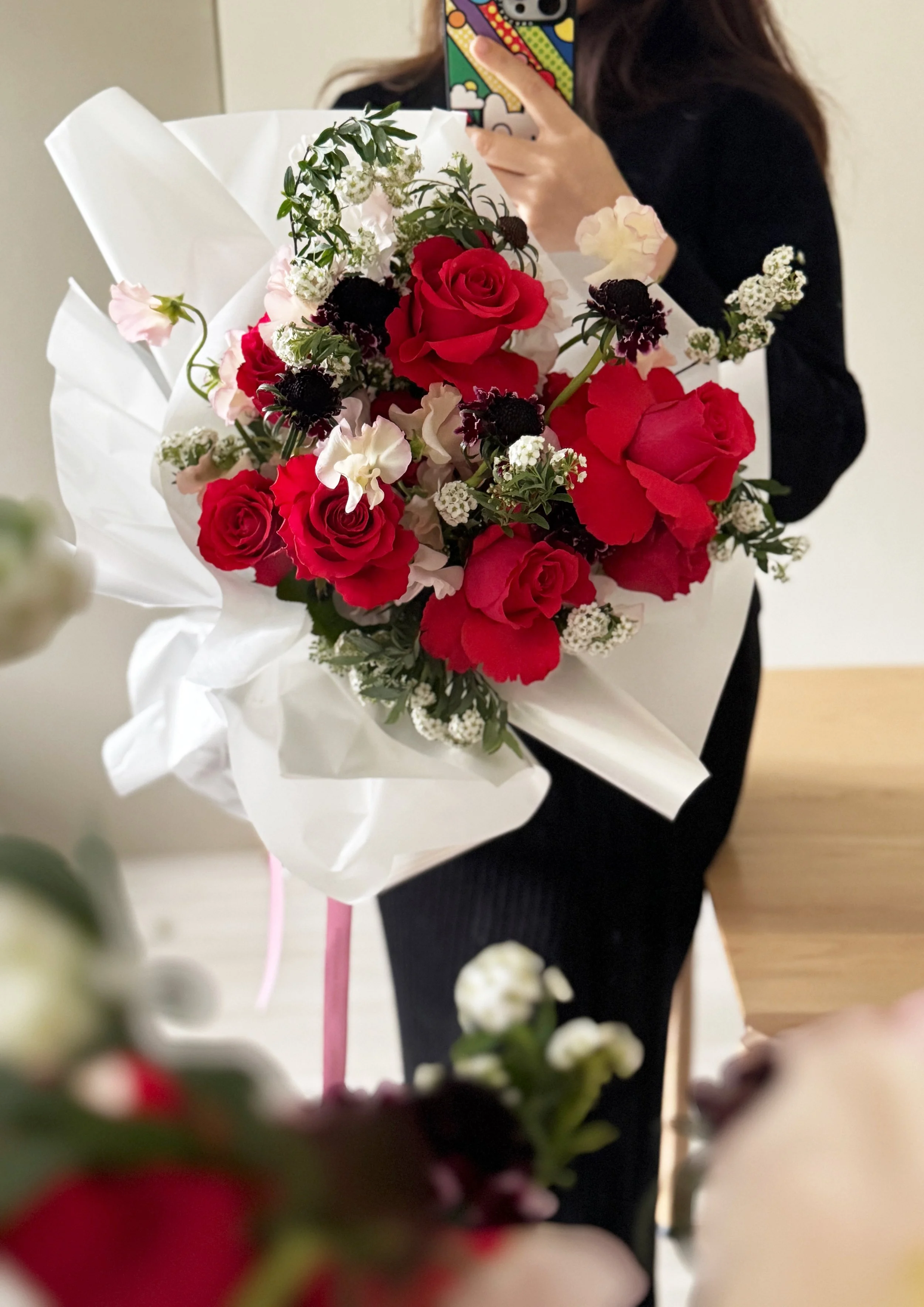 Person holding a large bouquet of red roses, white and pink flowers wrapped in white paper, with someone taking a mirror selfie.