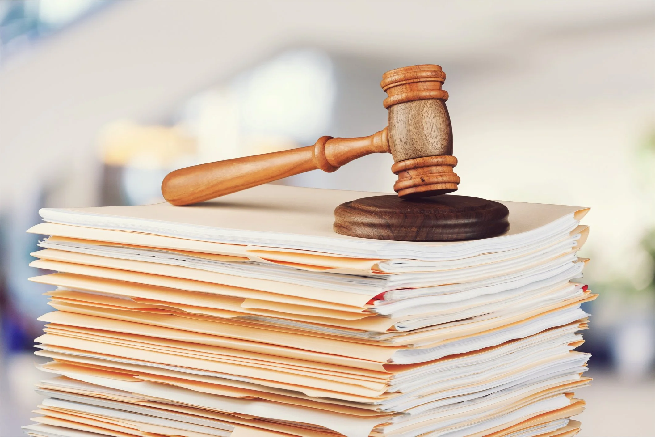 A wooden gavel resting on a large stack of papers in an office or courtroom setting.
