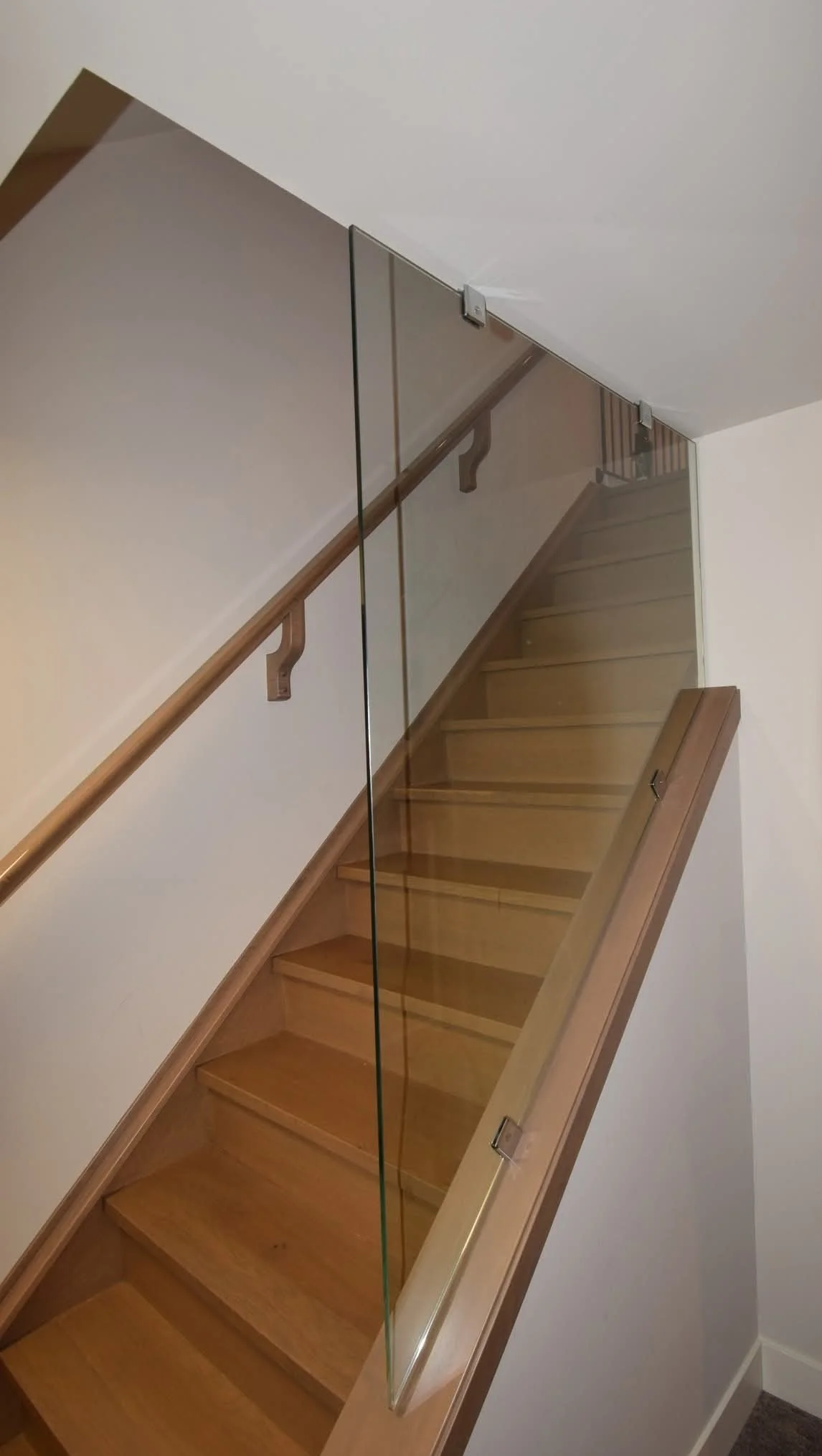 Wooden staircase with glass safety barrier on the side, ascending to an upper floor.