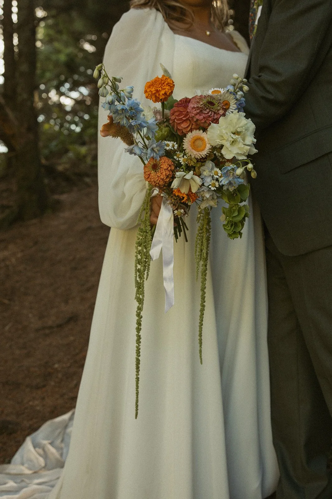 A bride in a white wedding dress holding a colorful bouquet of flowers during a wedding ceremony outdoors.