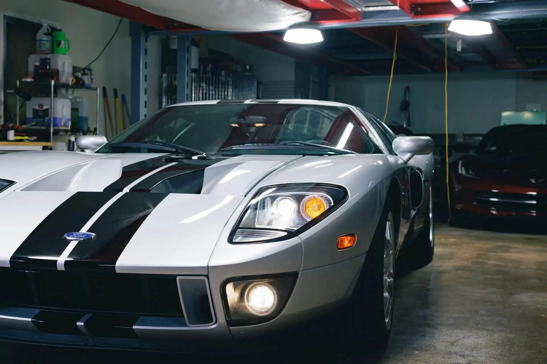 A silver Ford GT sports car with black racing stripes parked inside a garage or workshop.