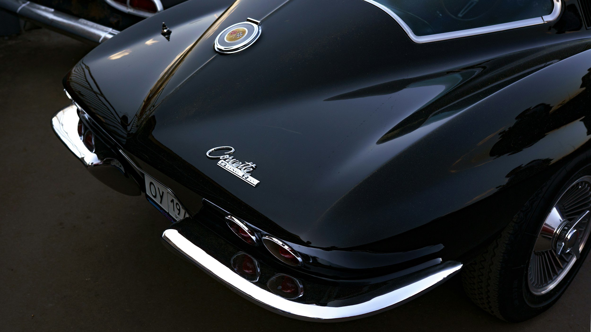 Black Chevrolet Corvette Stingray with a shiny exterior, rear view, showing taillights, Corvette badge, and a European license plate.
