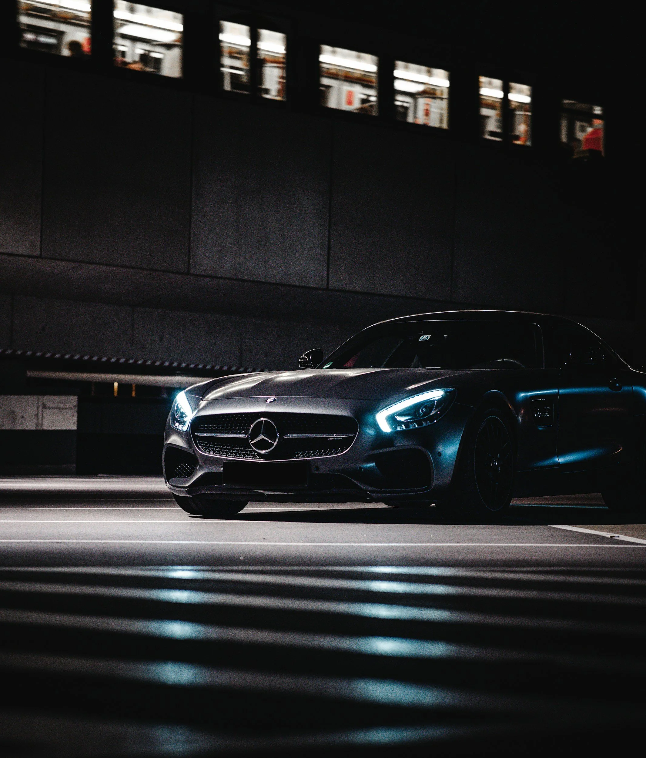 Black Mercedes-Benz sports car parked in an urban parking structure at night with lit headlights.