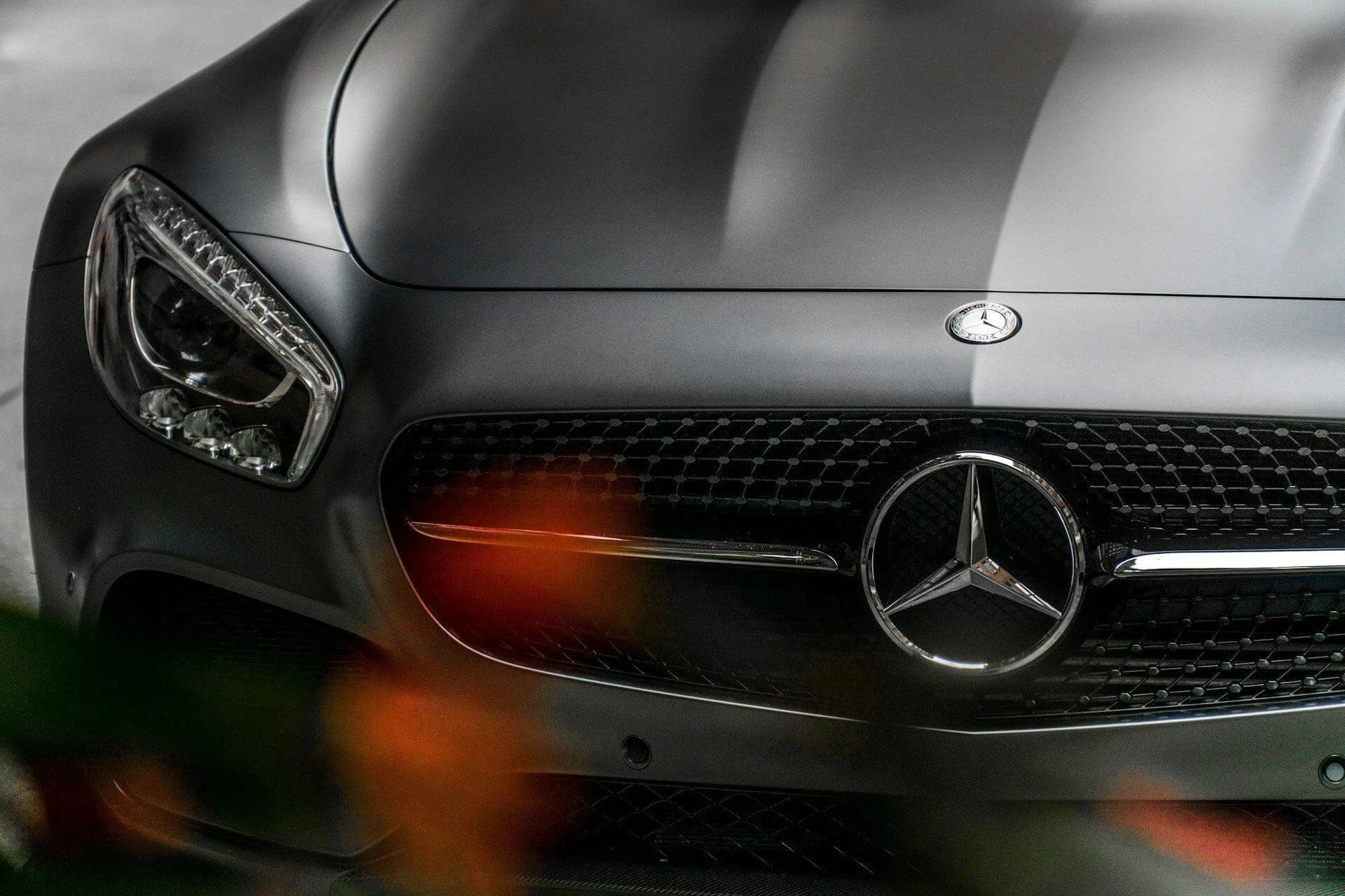 Close-up of the front of a matte gray Mercedes-Benz car, showing the headlight, grille, and Mercedes-Benz logo.