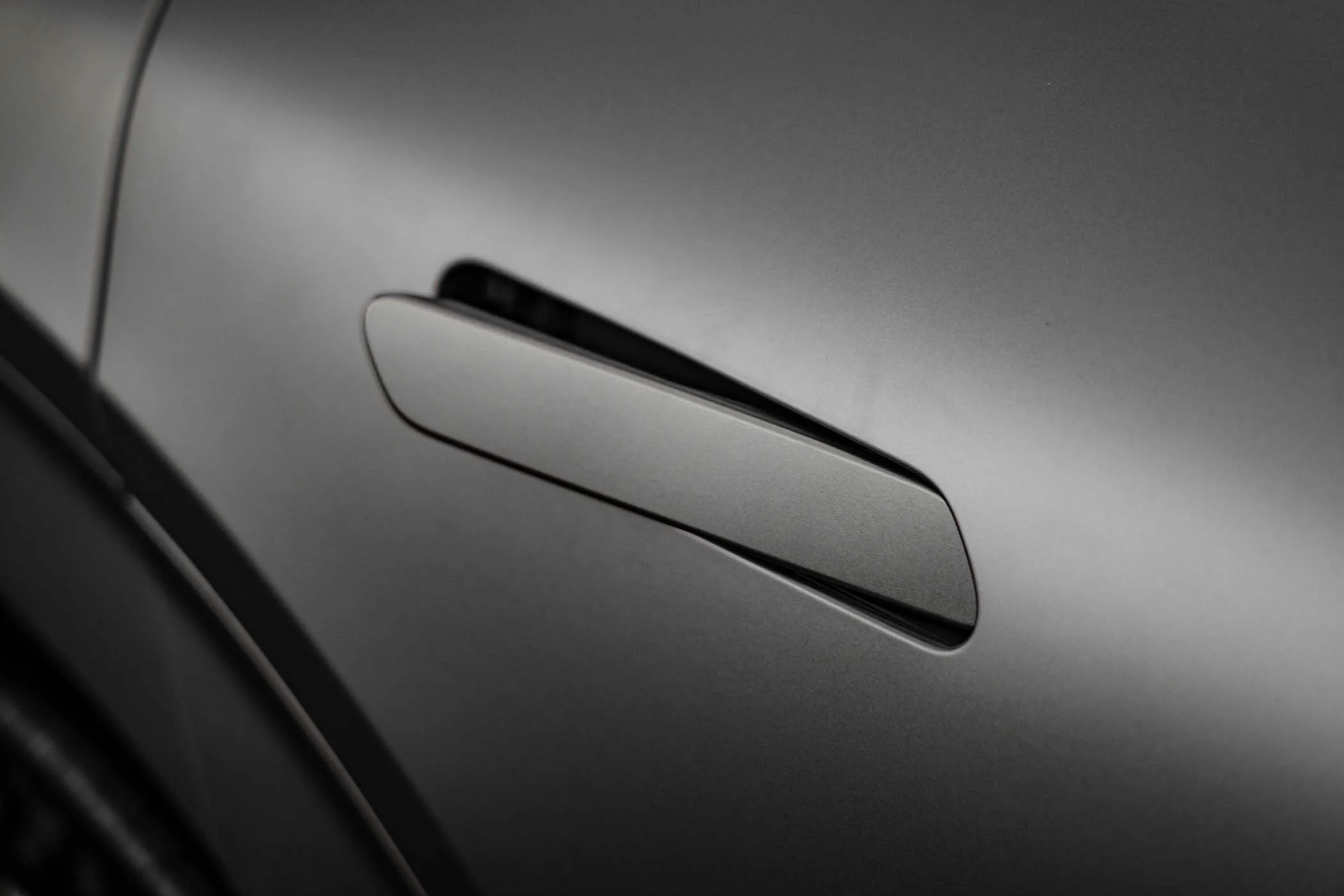Close-up of a silver car door handle on a gray vehicle.
