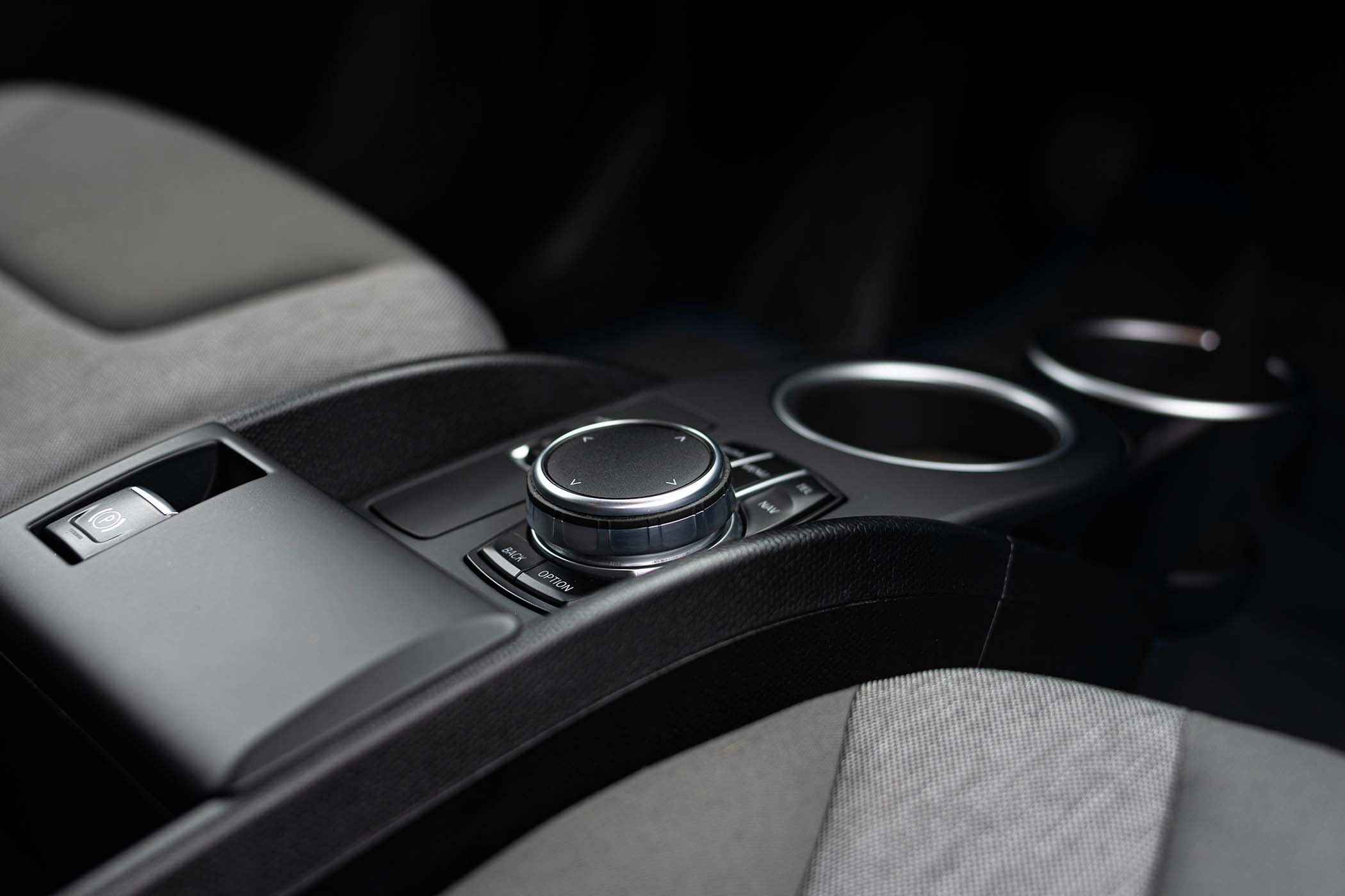 Close-up of a car's center console with a control dial, two cup holders, and an electronic parking brake button.