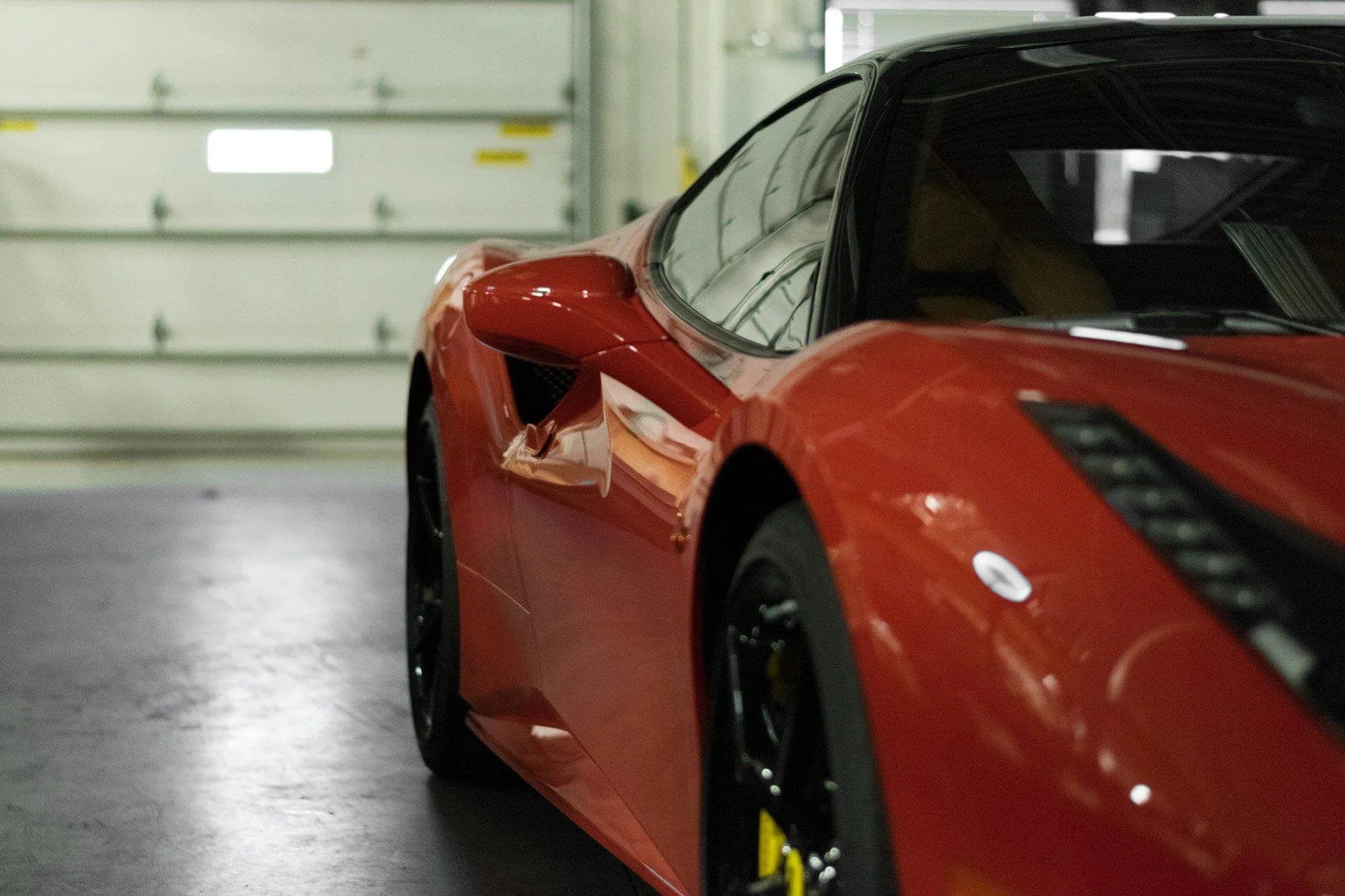 A red sports car parked in a garage with a closed white garage door in the background.
