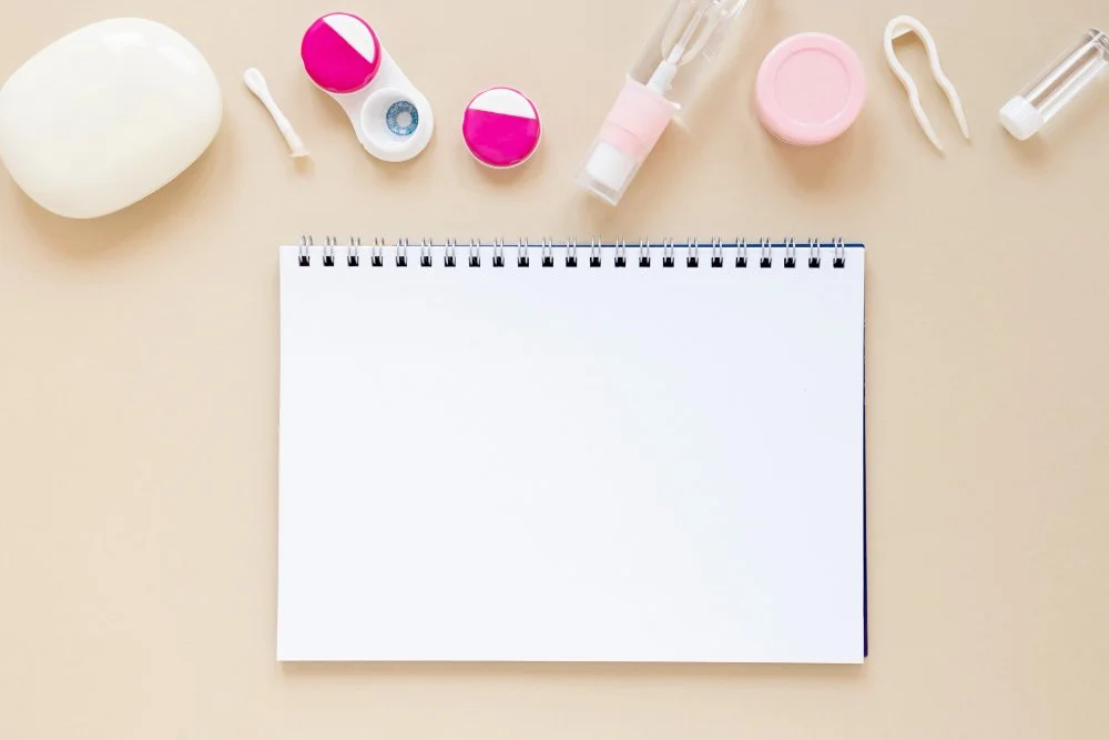 Flat lay of beauty and skincare products around a blank notebook on a beige background.