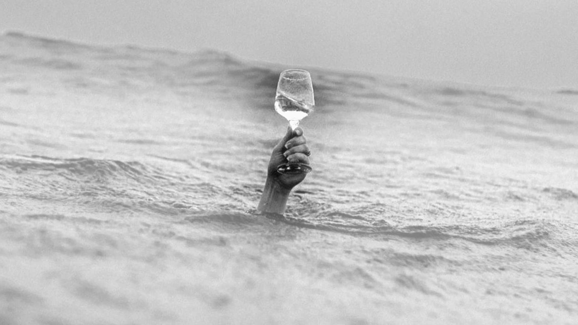 A hand holding a wine glass is emerging from the water in the ocean.