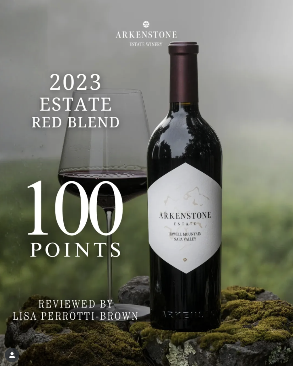 A bottle of Arkenstone estate winery 2023 estate red blend wine next to a glass of red wine on a moss-covered rock with a blurry outdoor background.