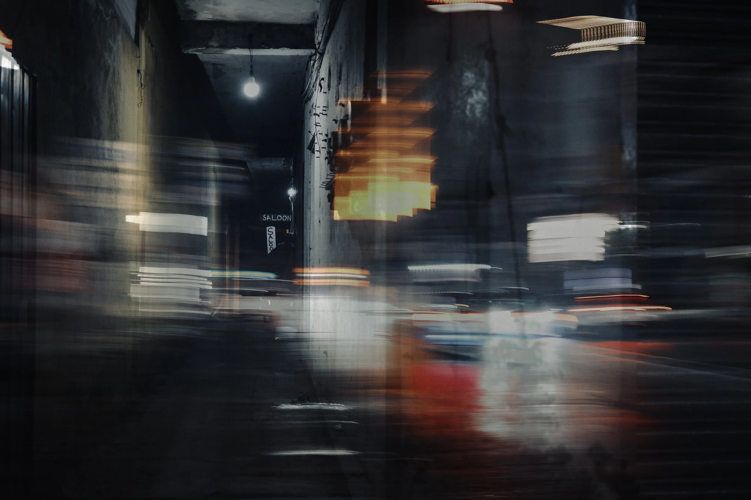 Blurred motion photo of a city street at night with lights and a sign that reads 'Saloon' on the side.