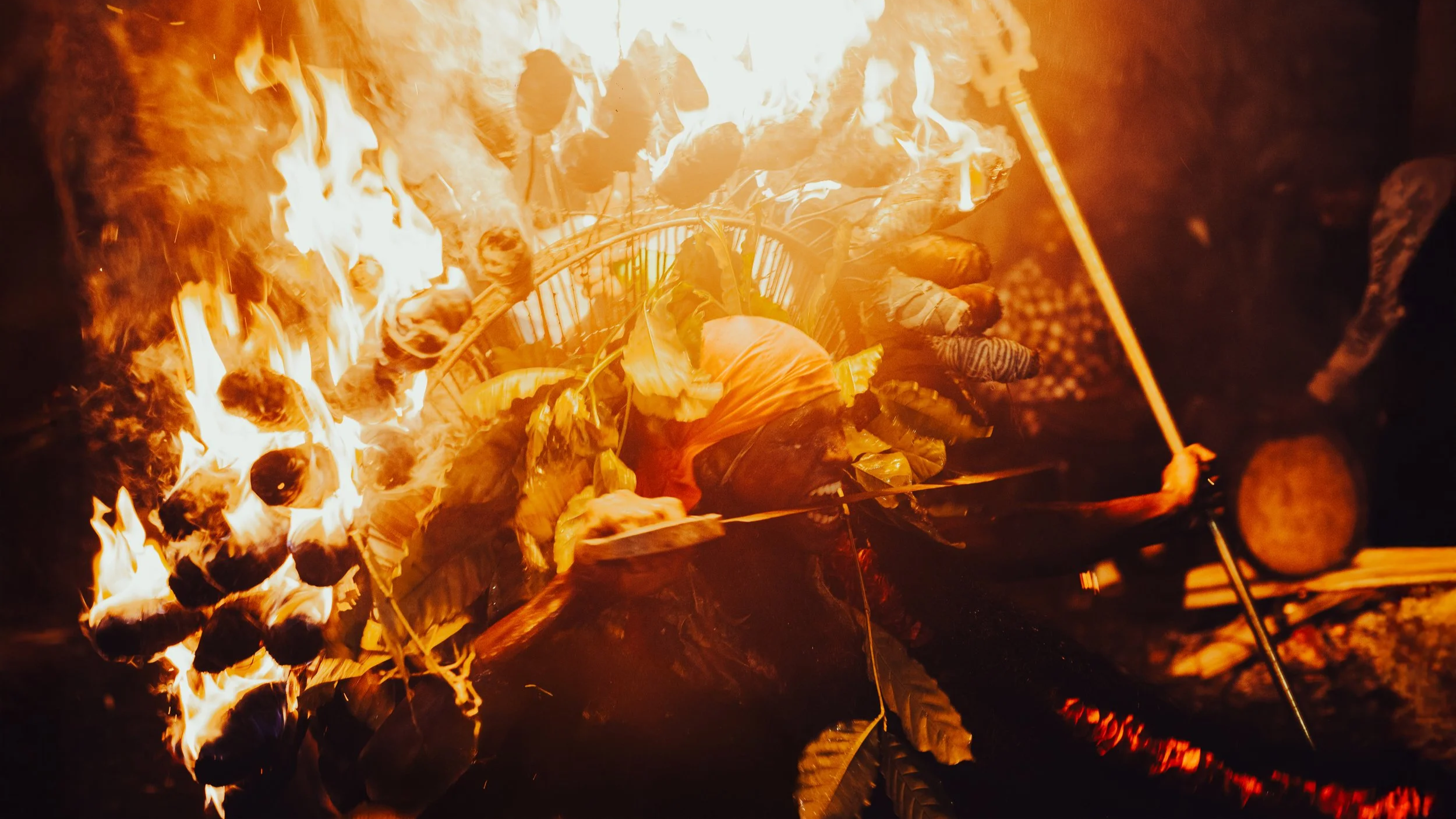 A person standing in front of an outdoor campfire at night, roasting marshmallows and cooking food over flames.