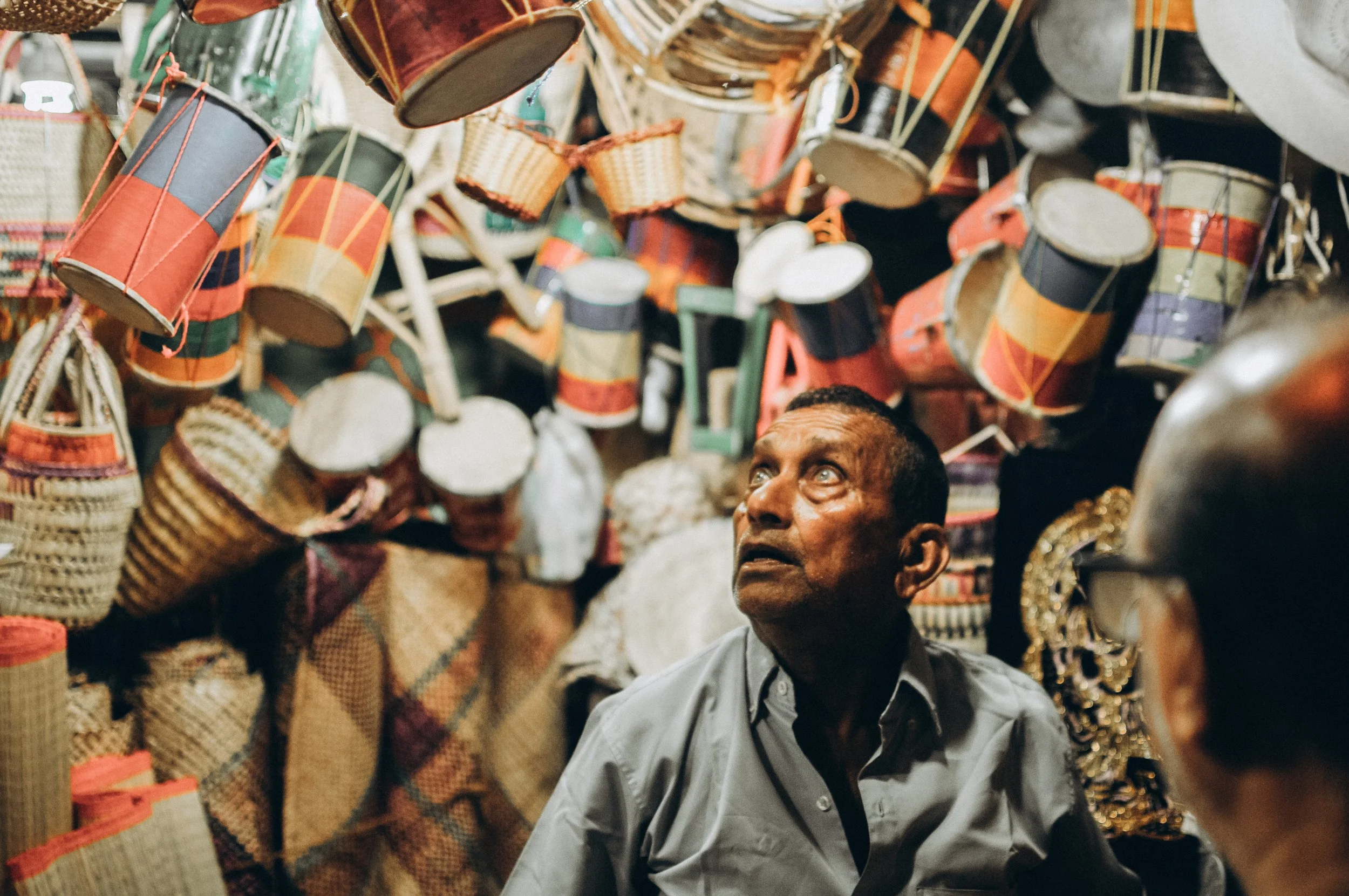 A man shopping for woven baskets and containers at an outdoor market, with various colorful baskets hanging overhead.