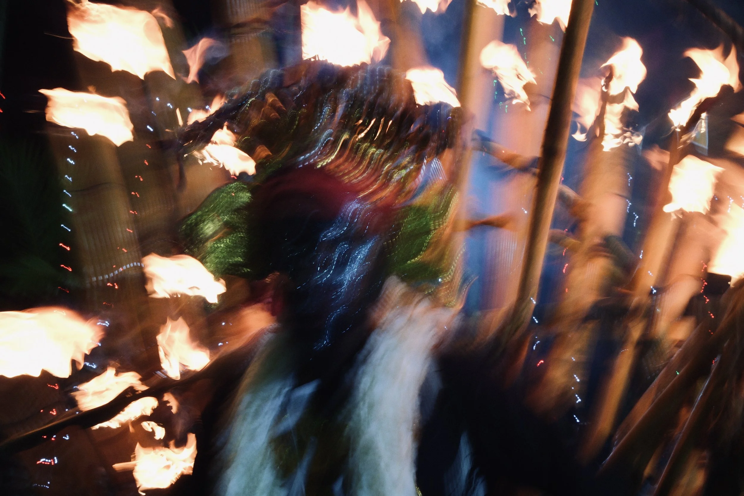 Blurred image of a fire show or performance, with flames and people holding sticks with fire at night.