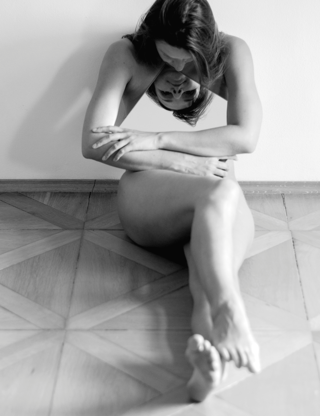 Black and white photo of a woman sitting on the floor, with her arms crossed and her head down, reflecting a contemplative or pensive mood.