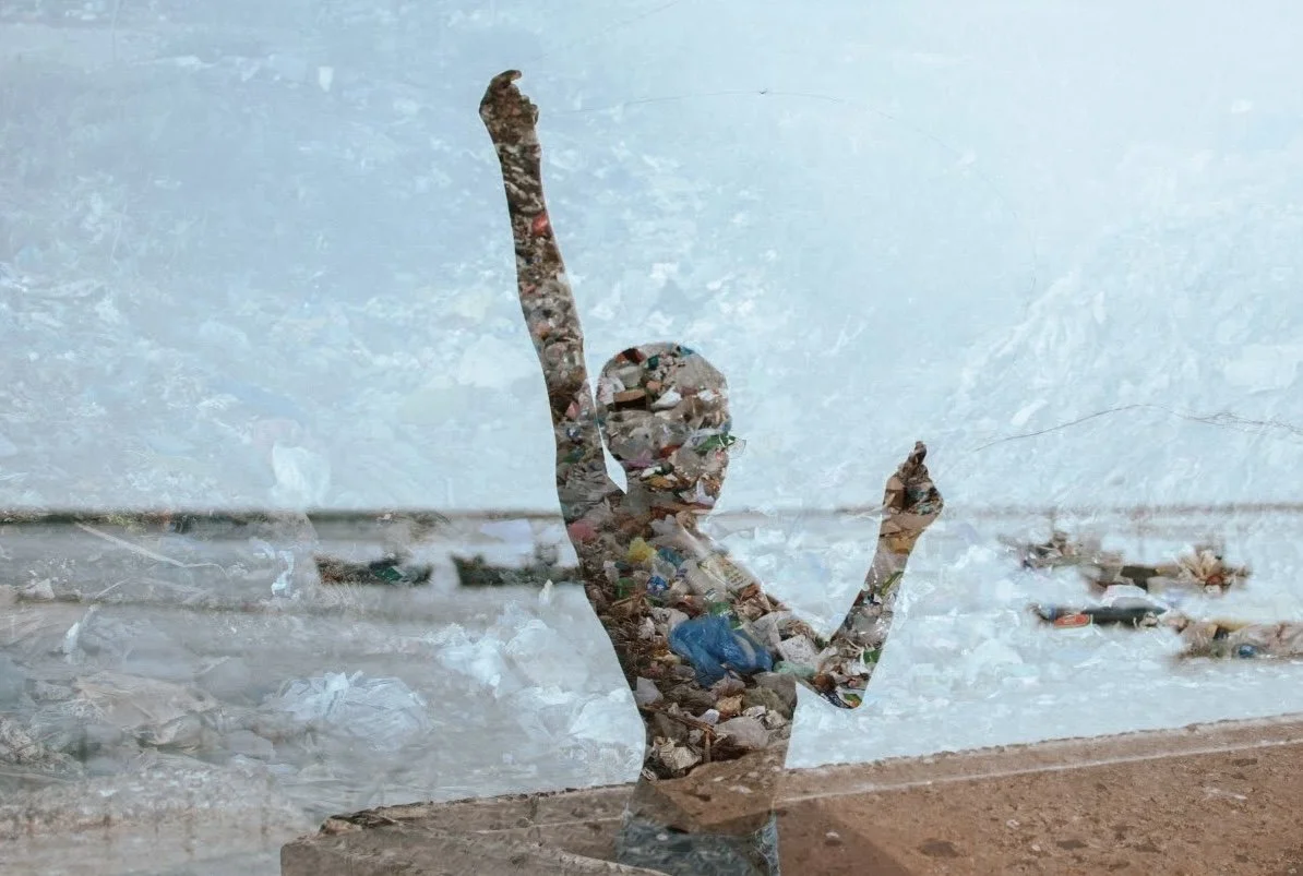 A person holding a smartphone with a background of a landfill filled with trash, seen through a glass window, creating a layered effect.