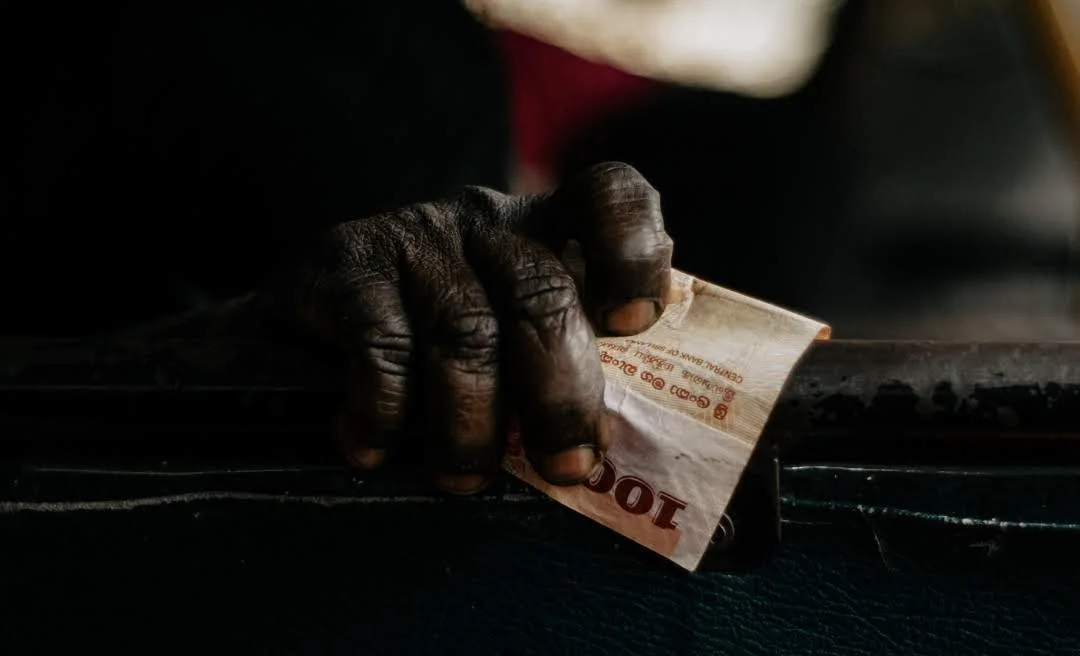 A dark-skinned hand holding a 10 rupees note and placing it into a black surface or a small box.