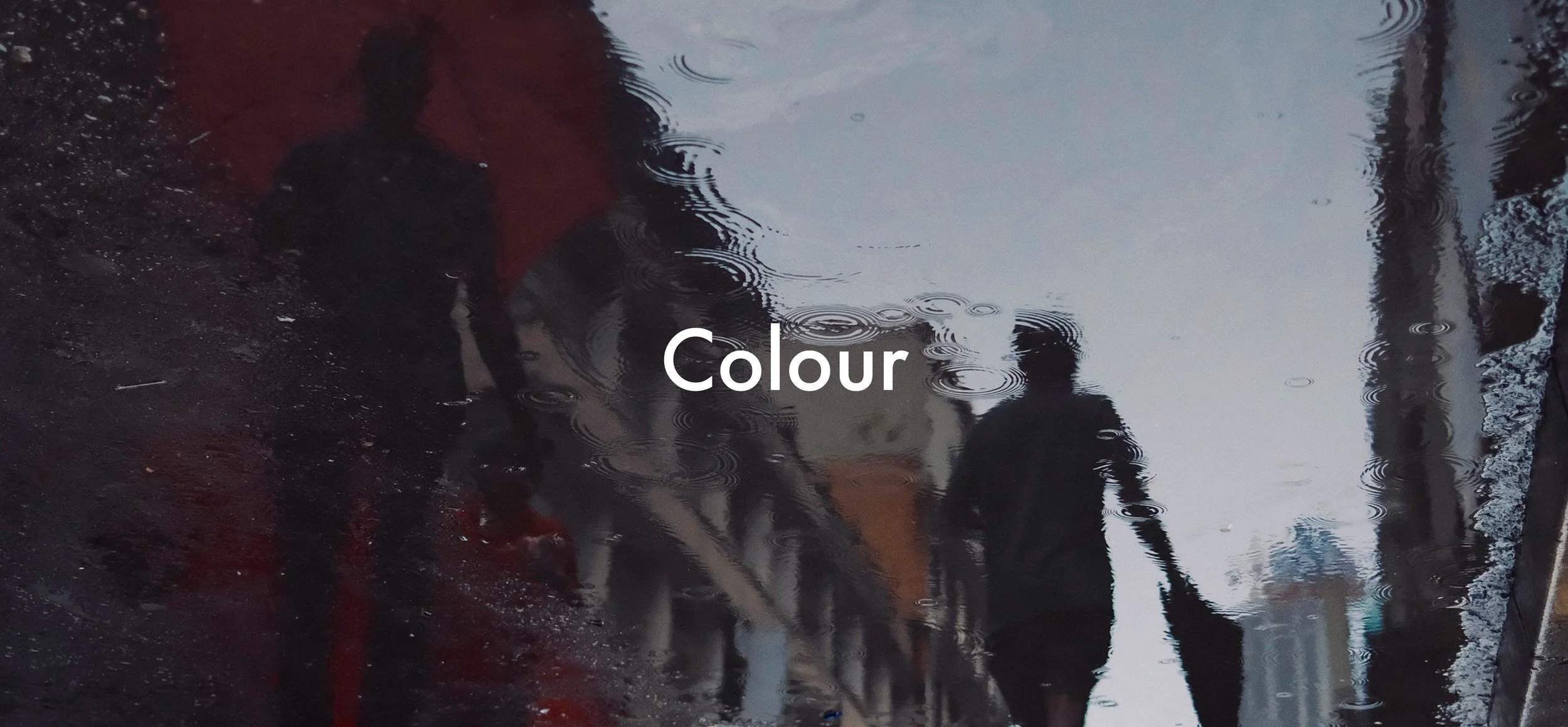 Reflected image of a rainy street scene with puddles, buildings, and a pedestrian, with the word 'Colour' overlaid.
